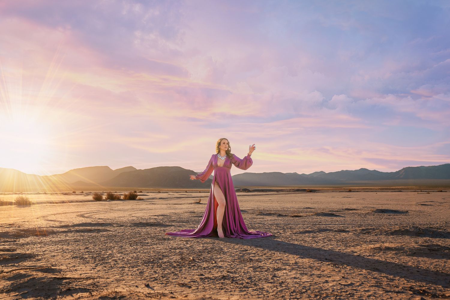 Desert landscape photoshoot with flowing pink gown against dramatic sunset sky.
