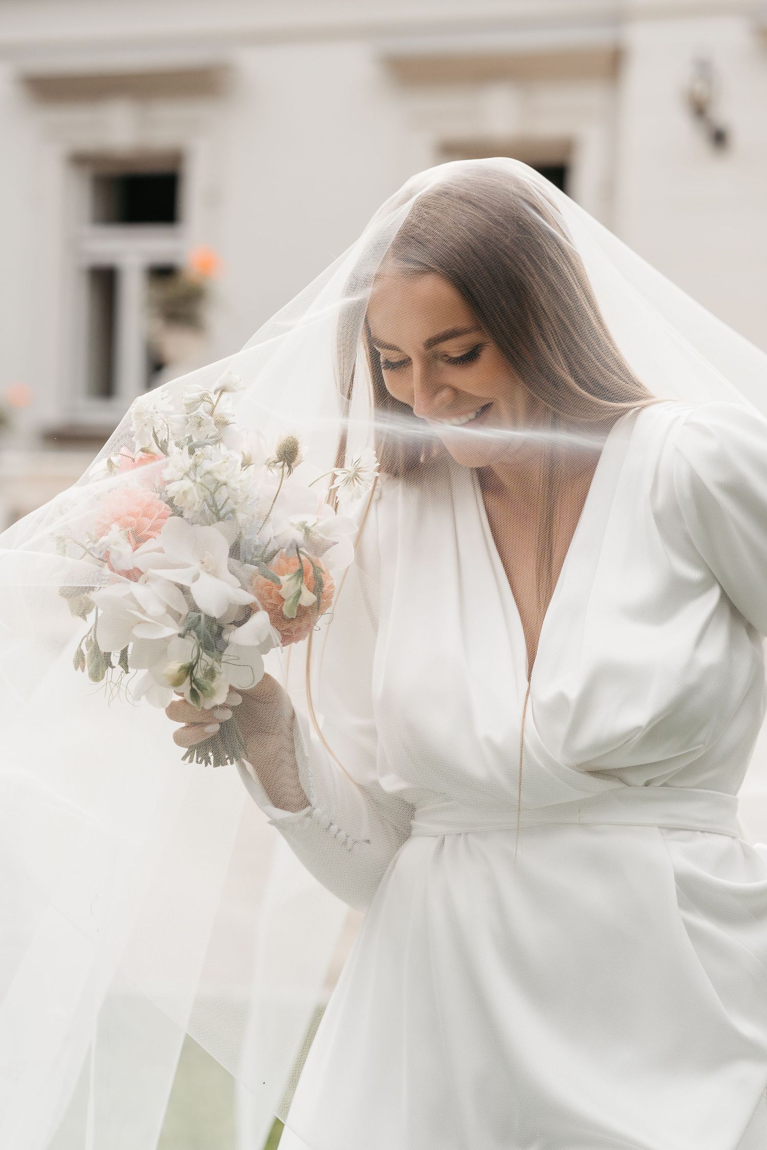 Bride in white wedding dress with billowing sleeves holds bouquet against light background in romantic bridal portraits.