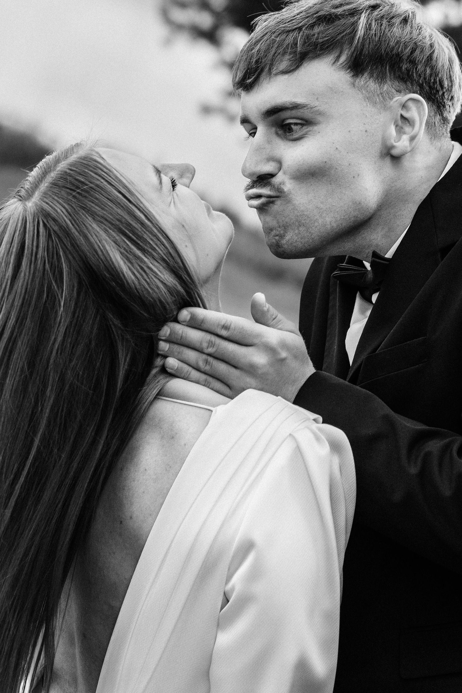 An intimate black and white portrait of a couple sharing a playful almost-kiss moment.