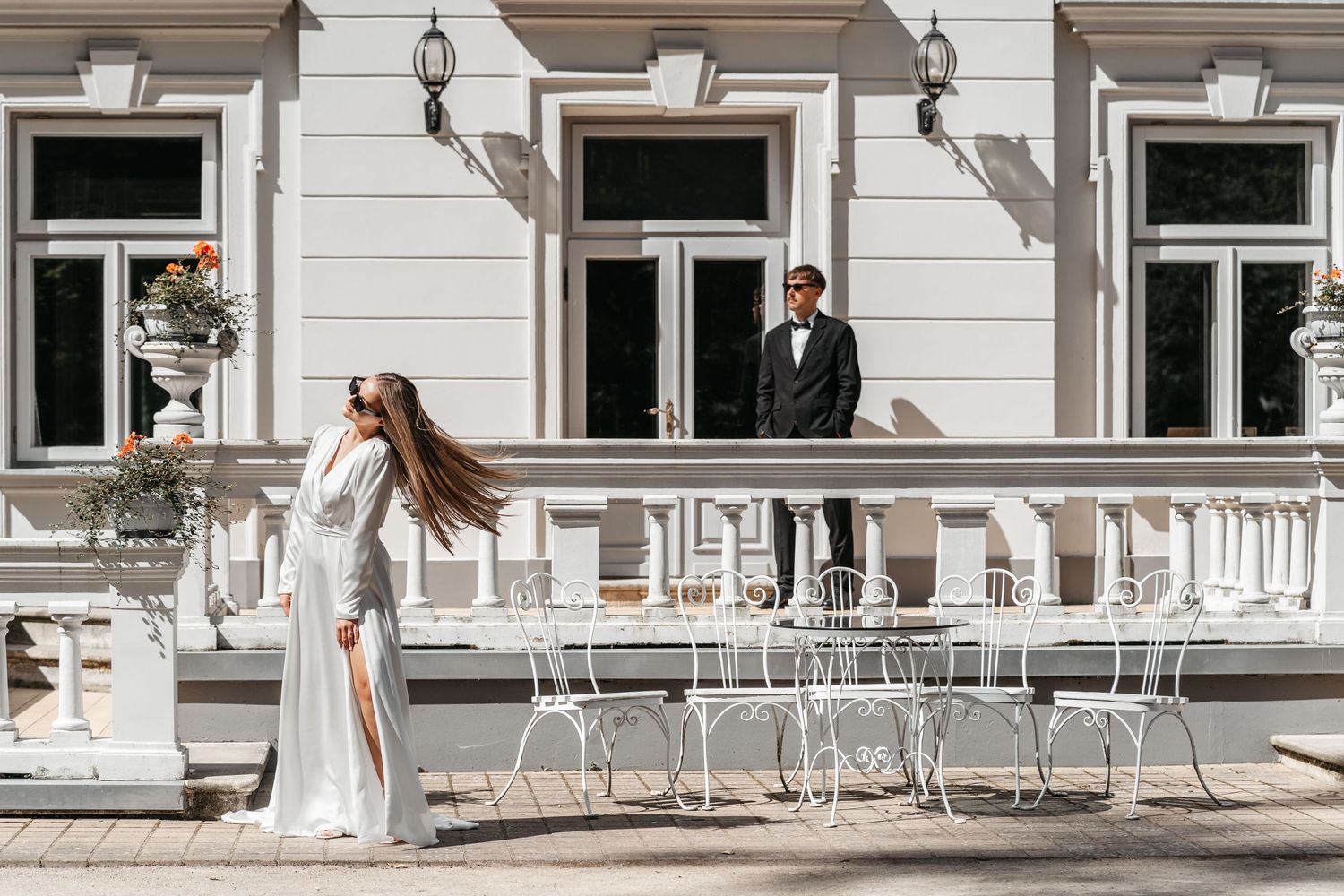 Stylish wedding couple on a white mansion terrace with vintage furniture.
