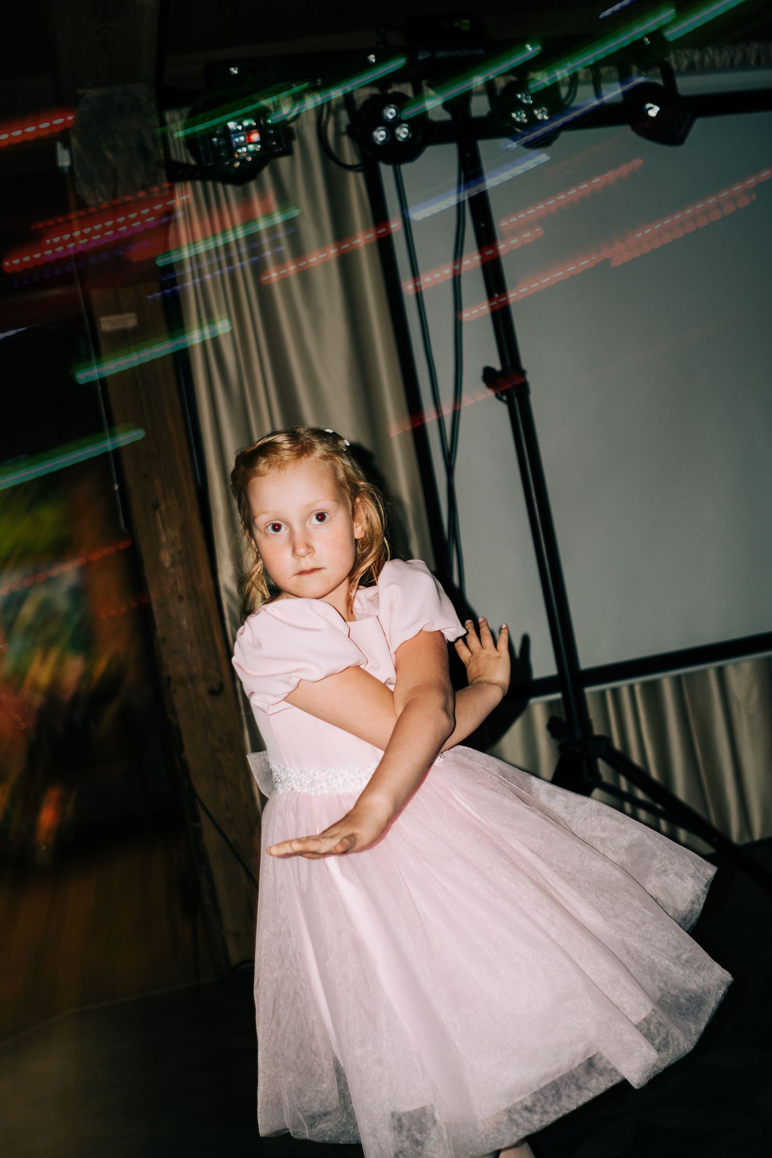 A child in a pink and white tulle dress twirls and dances in a dimly lit space with colored lights.