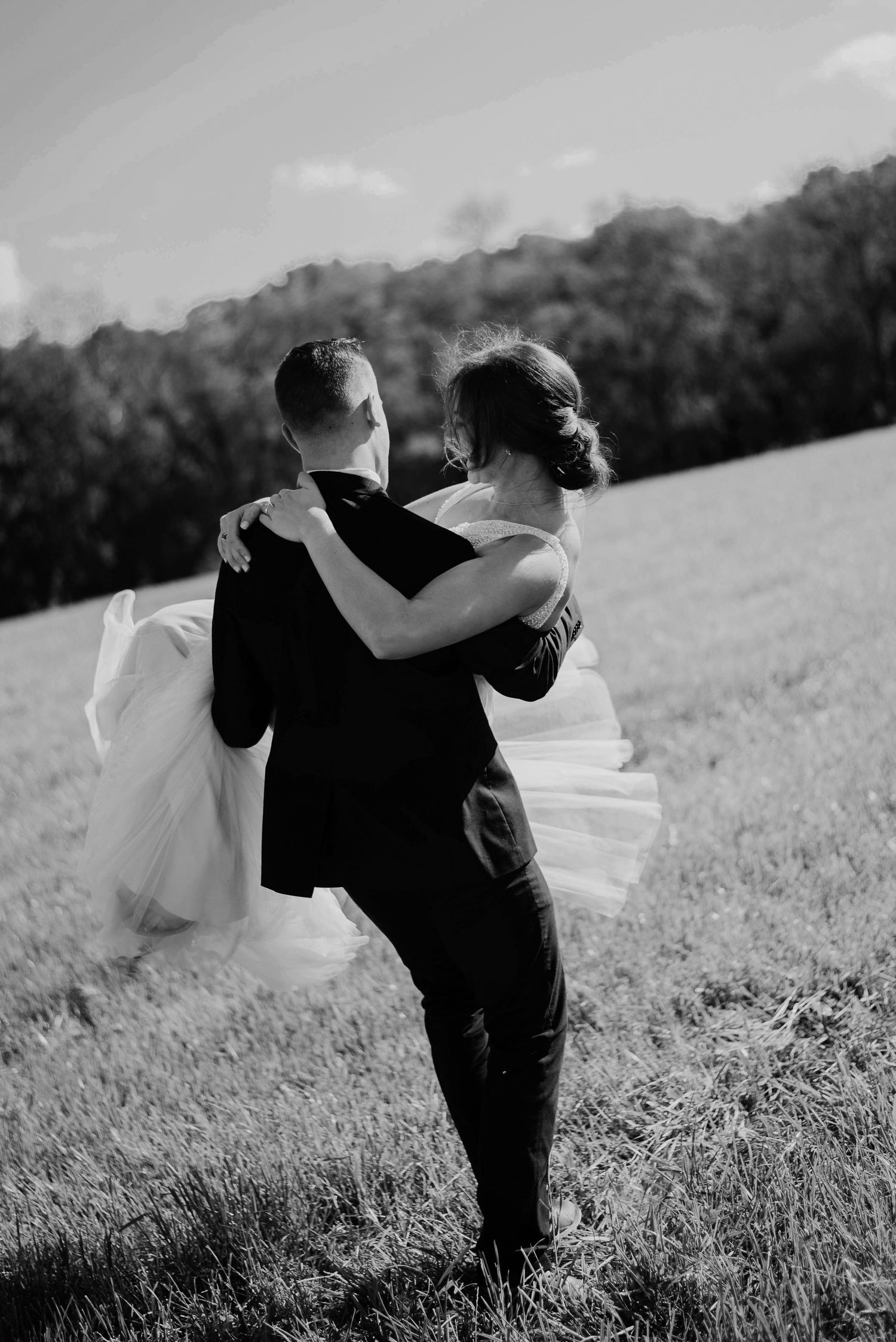A couple in wedding attire walks together across a grassy hillside in black and white.