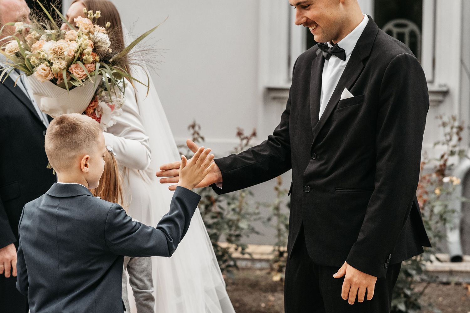 A young ring bearer in a navy suit gives a high five during an outdoor wedding ceremony.