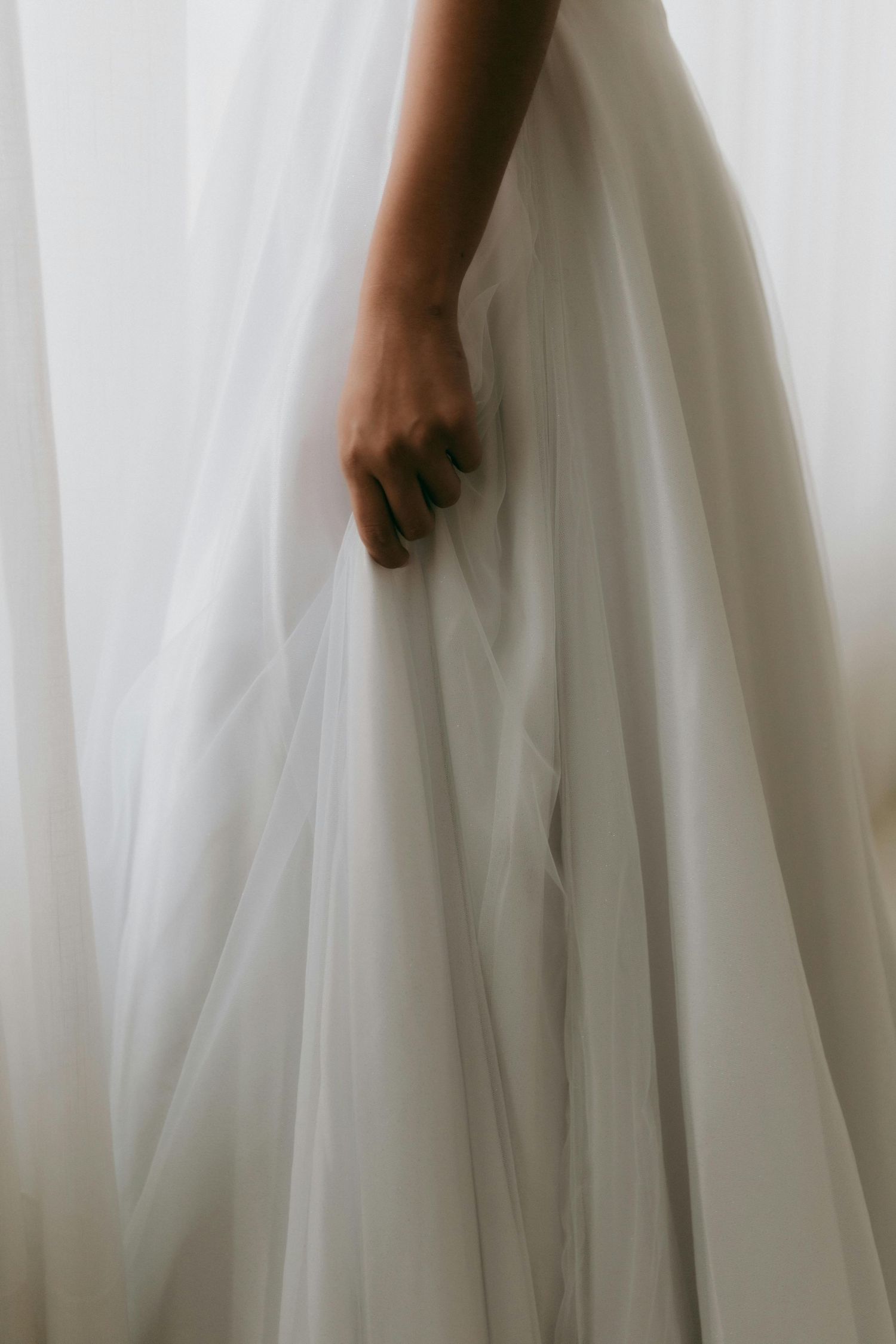 A hand gently holds flowing white wedding dress fabric against a soft, dreamy background.