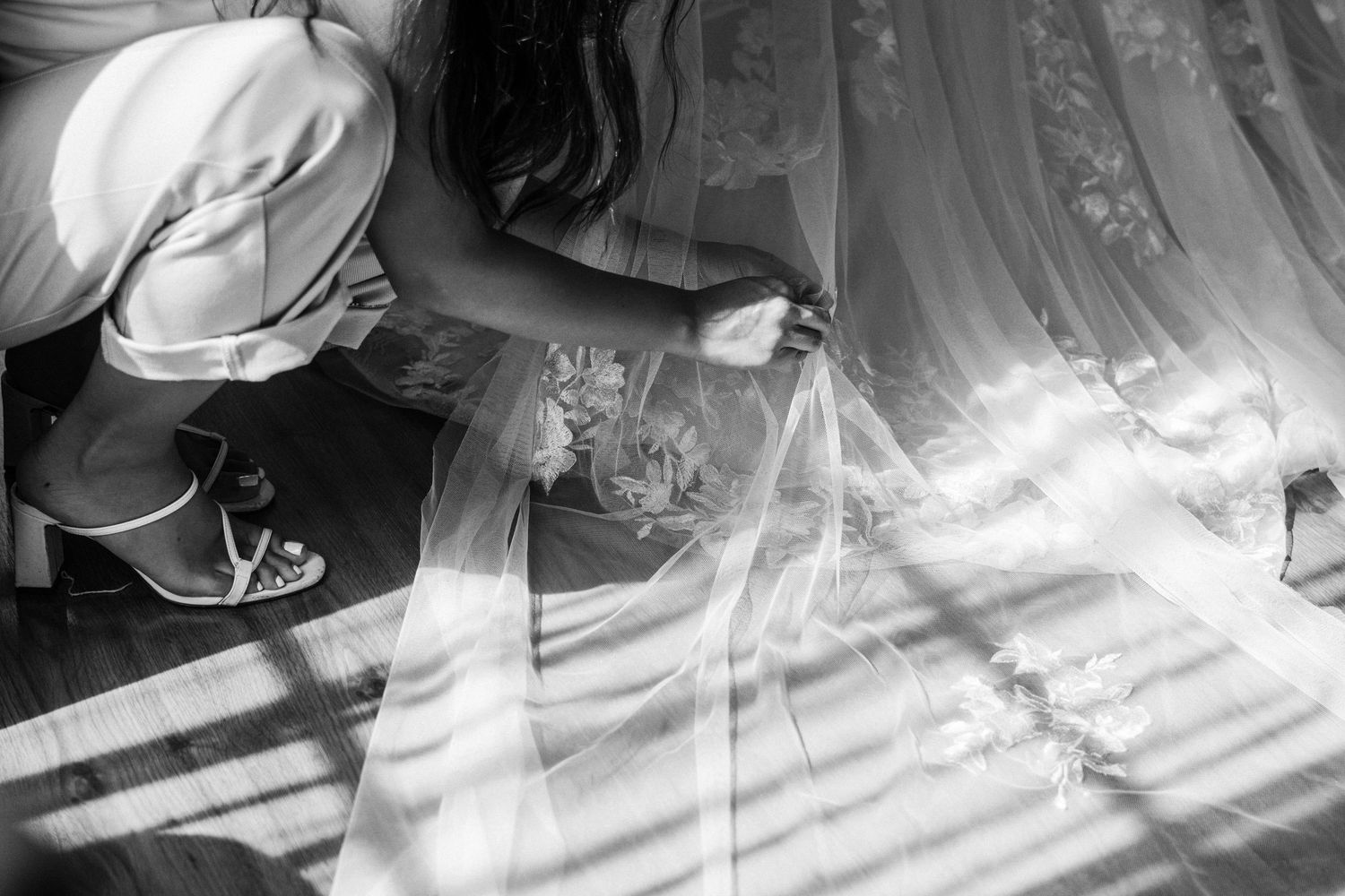 Black and white photo of sunlight streaming through sheer curtains onto a floor with scattered objects.