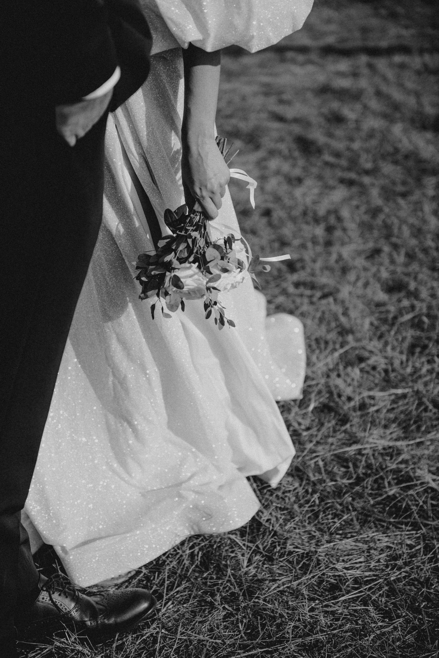Close up of white wedding dress hem against grass in black and white.