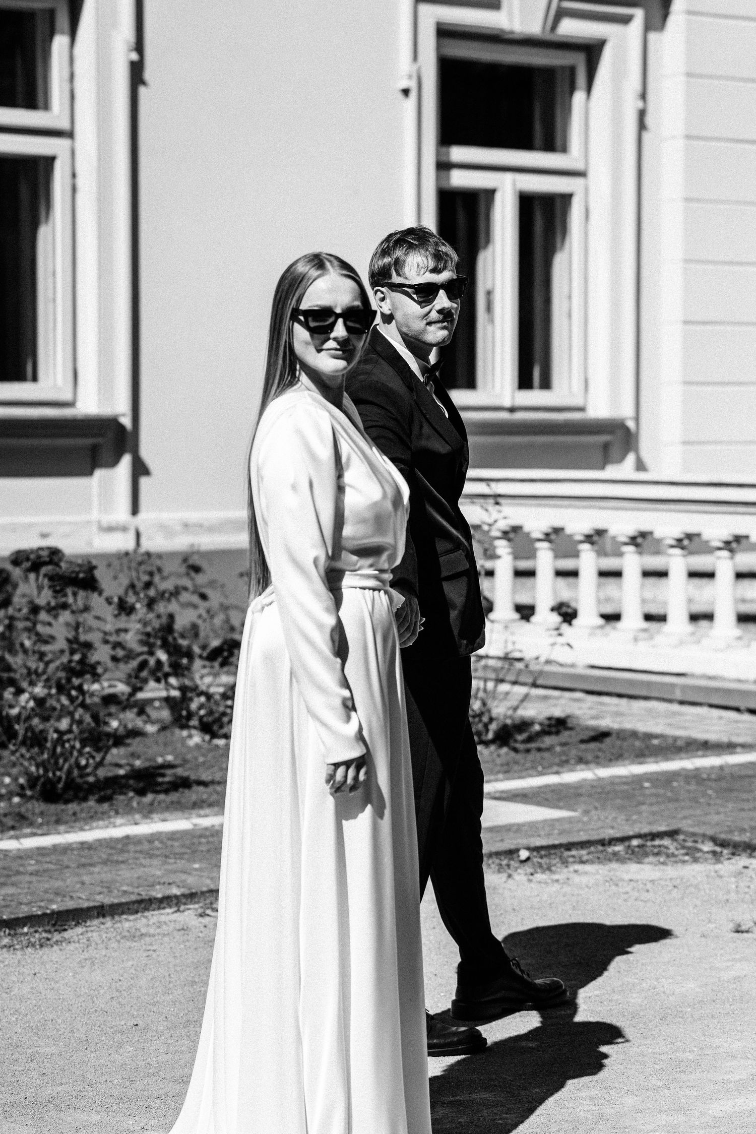 Black and white photo series of two people in contrasting outfits standing together in front of a building.