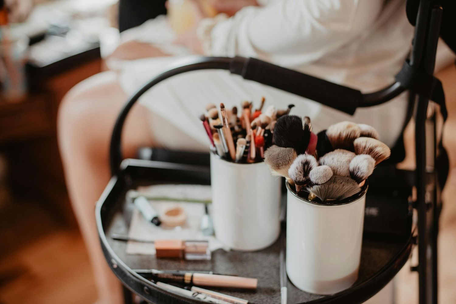 Makeup brushes and beauty products arranged on a table in warm lighting during a professional photoshoot.