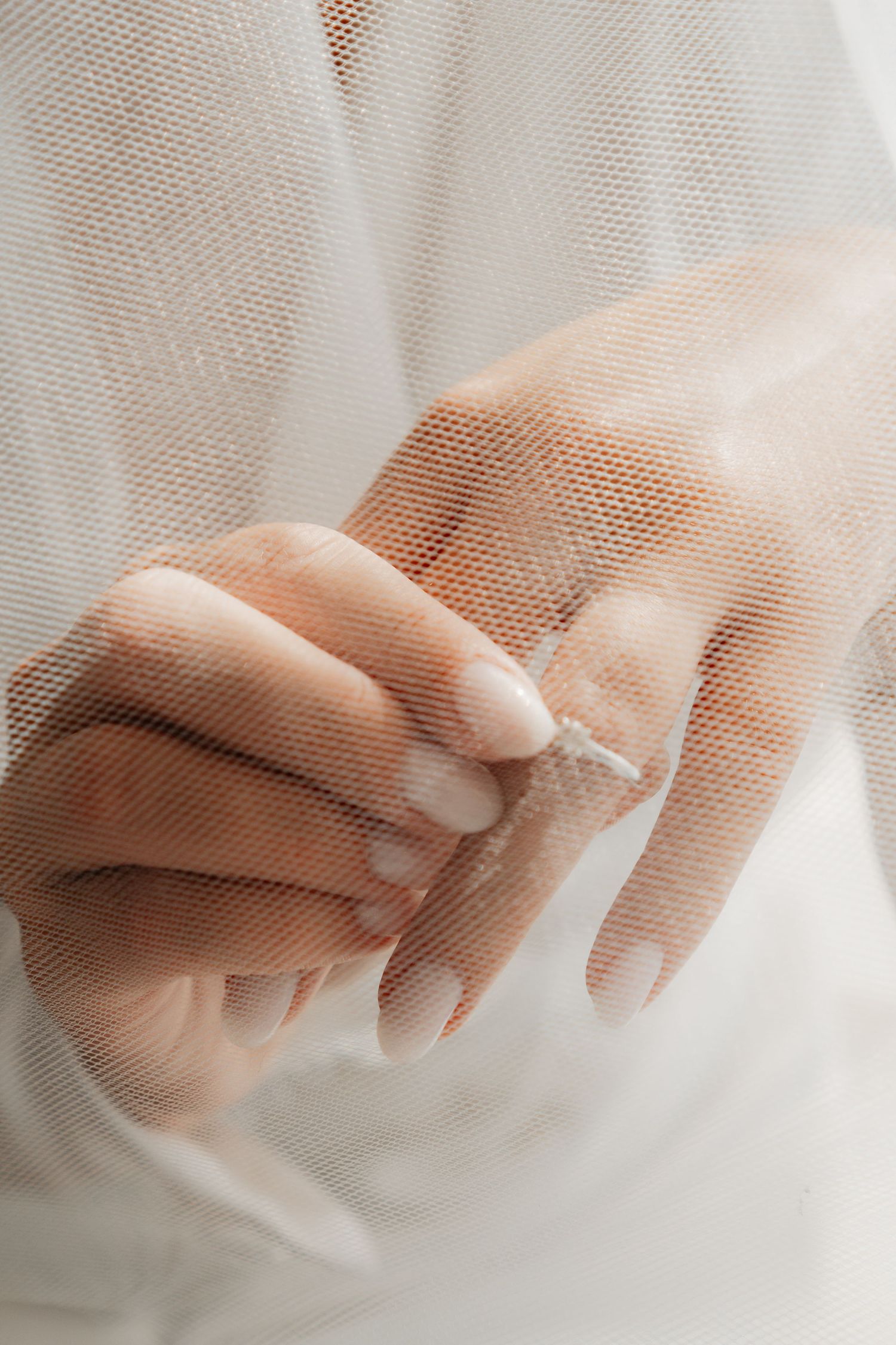 Delicate hands adjusting jewelry through sheer white veil fabric.