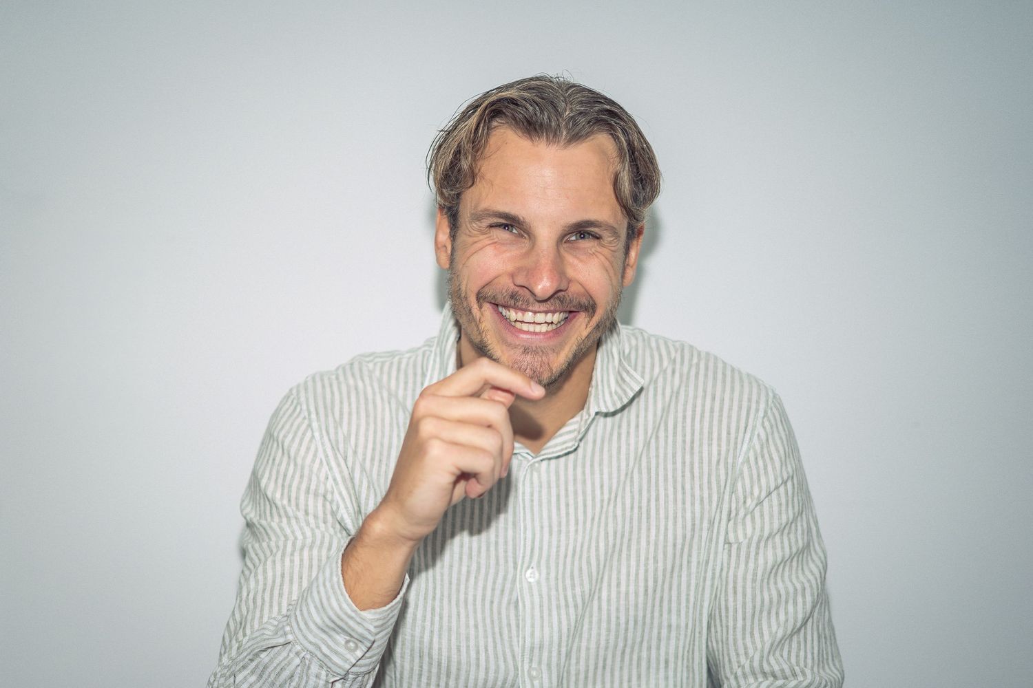 A person wearing a white sweater poses and smiles in a series of casual studio portraits against a light background.