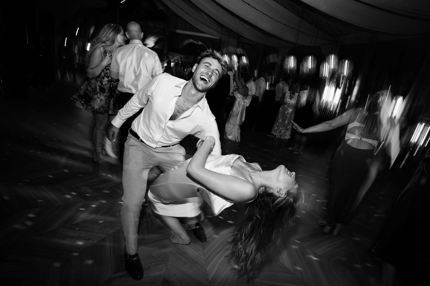 Dancers perform swing dance moves in a dimly lit venue with a crowd in the background.