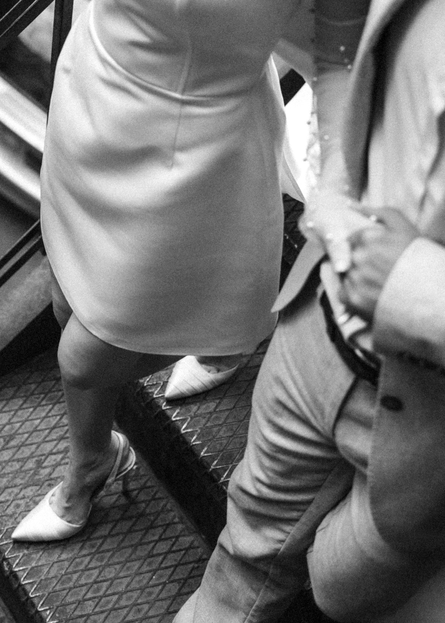 Black and white image of legs wearing white pants and shoes walking on a textured surface.