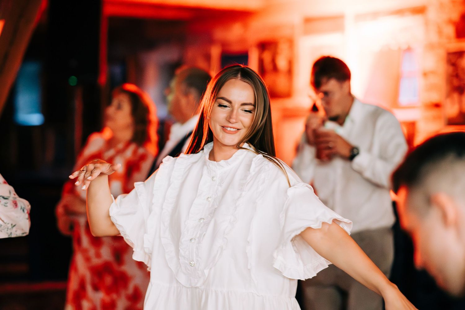 A group of wedding guests dance and celebrate on a vibrant red-lit dance floor at a reception party.