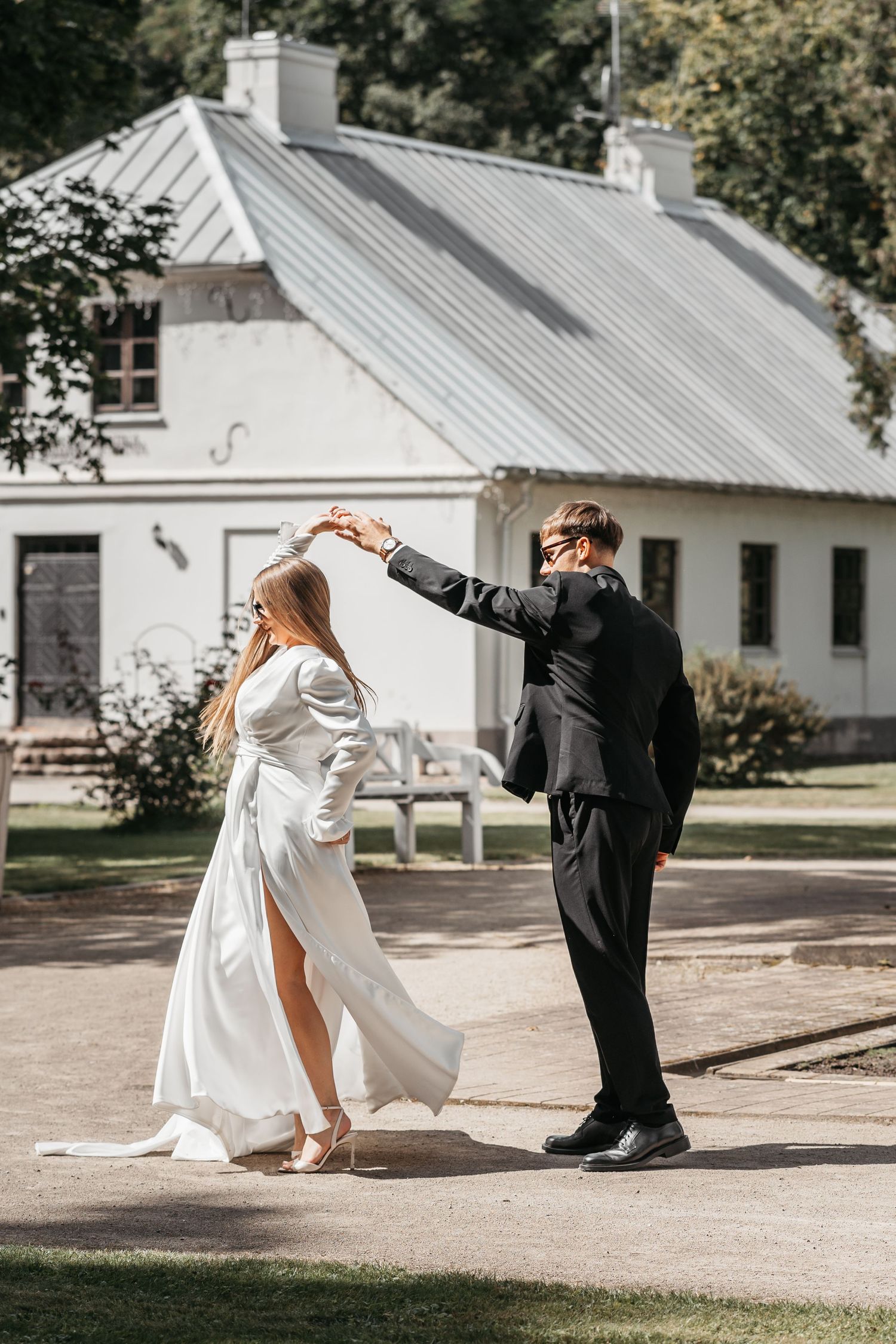 A playful wedding moment outside a white cottage with a couple in formal attire.
