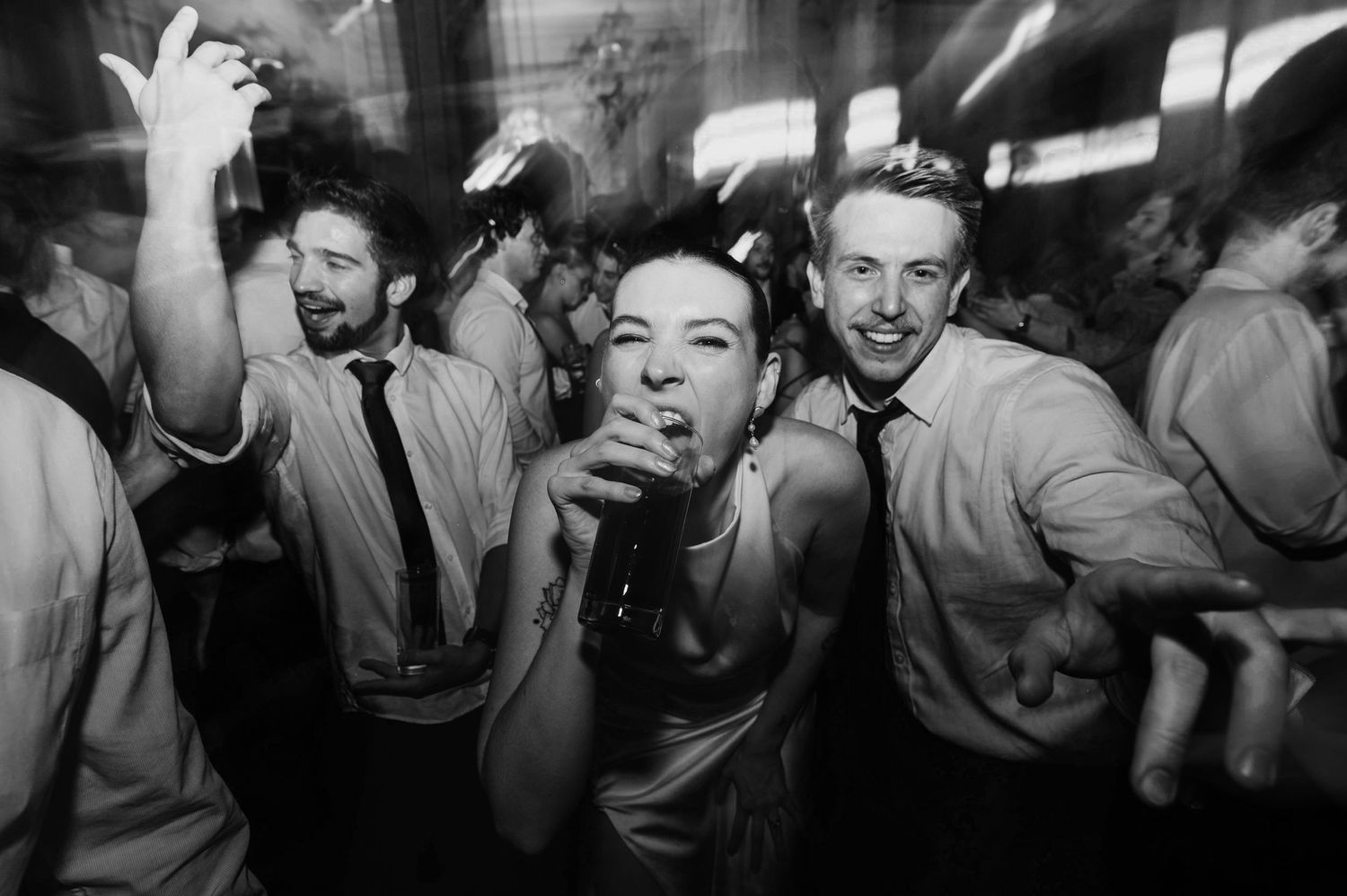 Black and white photograph showing energetic party scene with people dancing and celebrating in a crowded space.