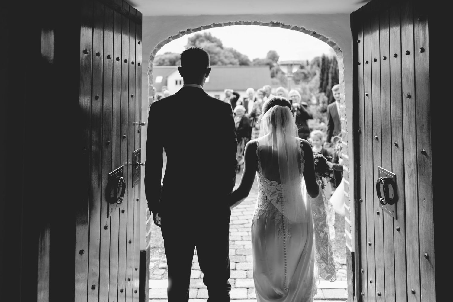 Wedding couple silhouetted in church doorway with Gothic wooden doors.
