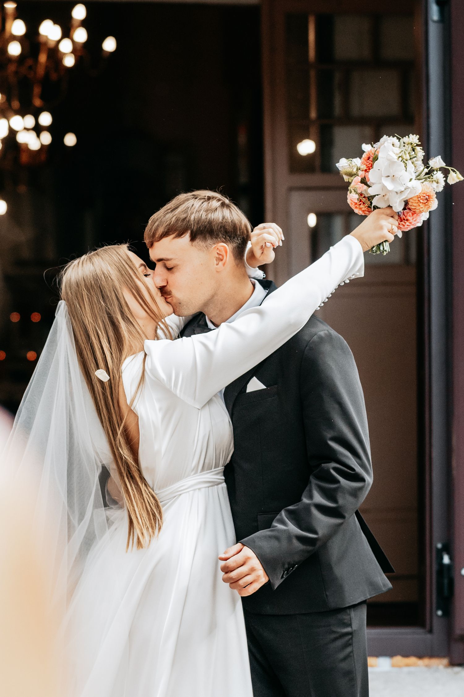 Romantic wedding moment captured in front of decorative doorway with string lights.