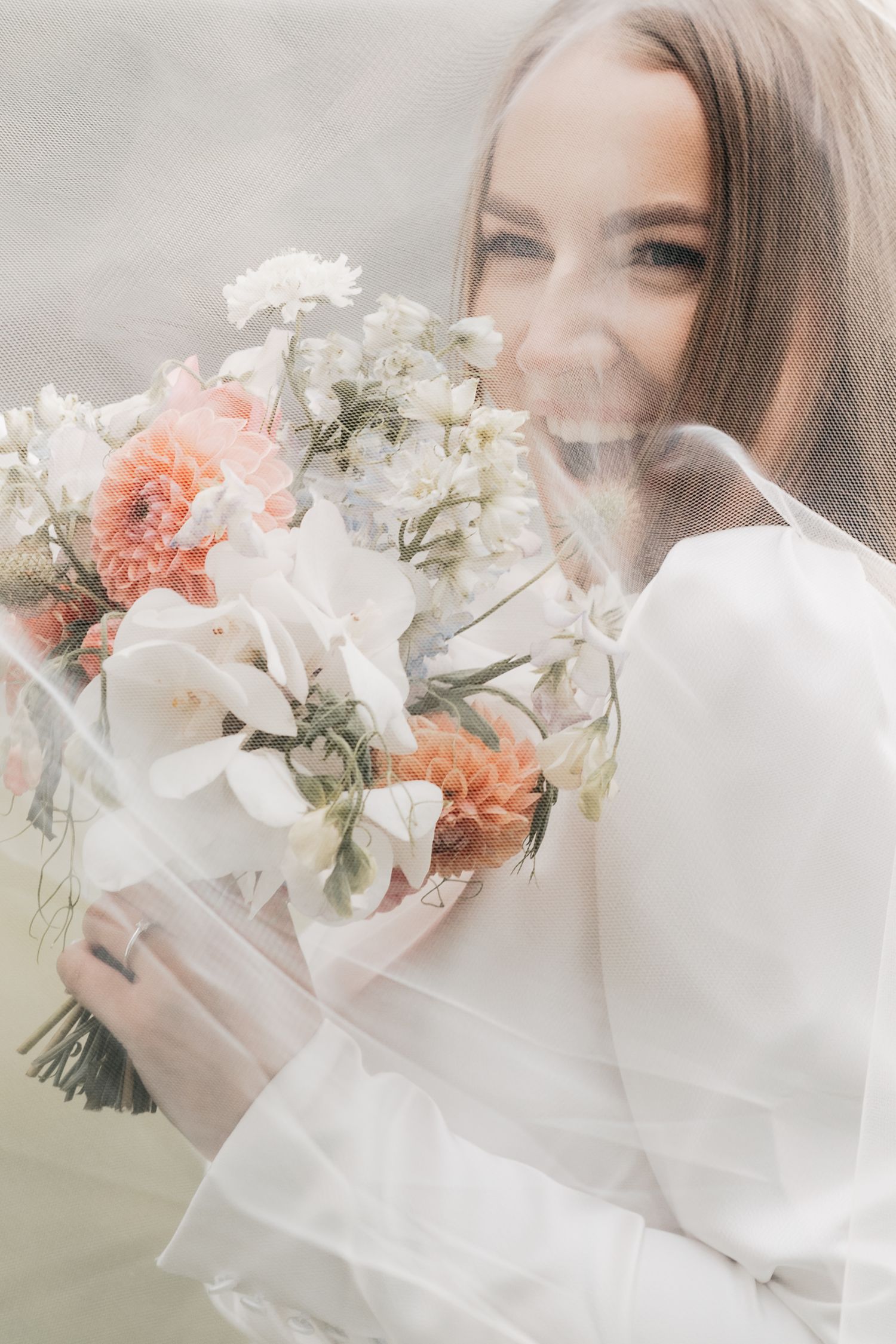 A dreamy bridal portrait series with soft white veil and coral flowers in natural light.