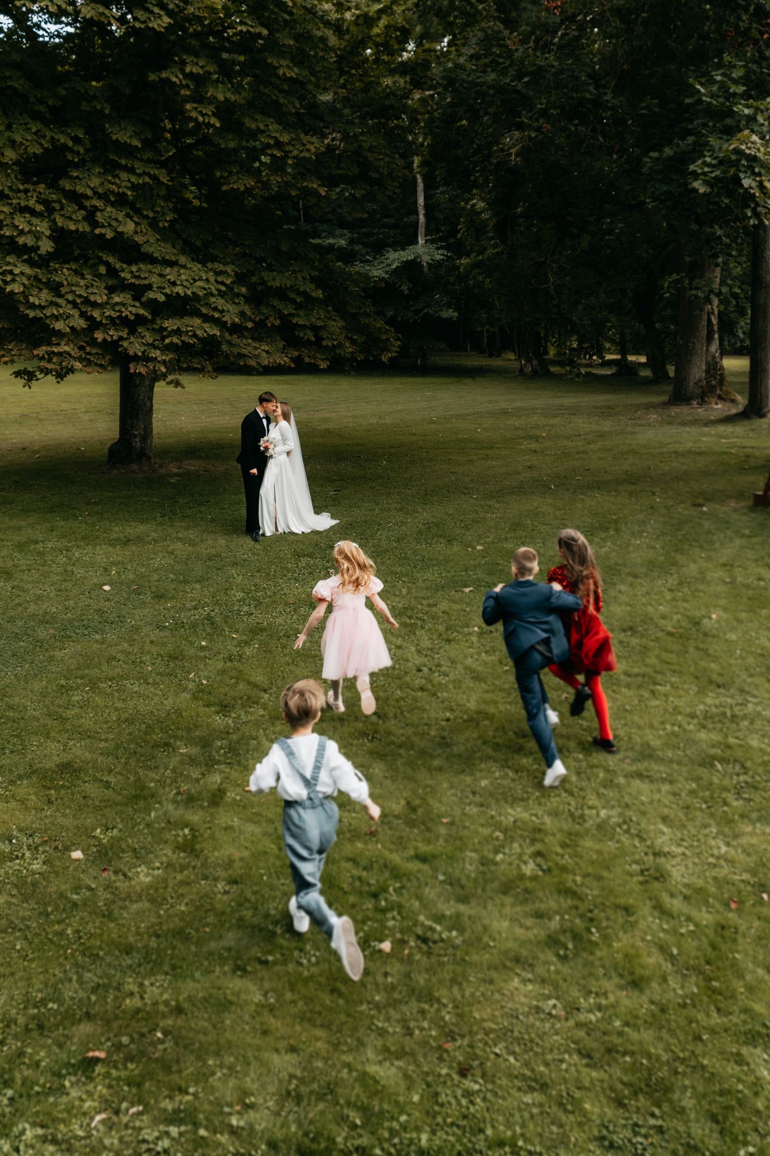 Children run and play together on a grassy lawn surrounded by trees in a sequence of connected photos.
