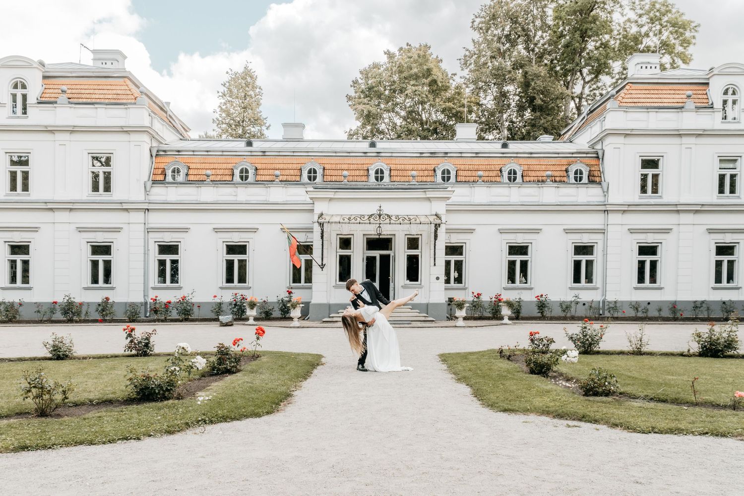 Wedding couple poses in front of a grand white historic mansion with symmetrical architecture.