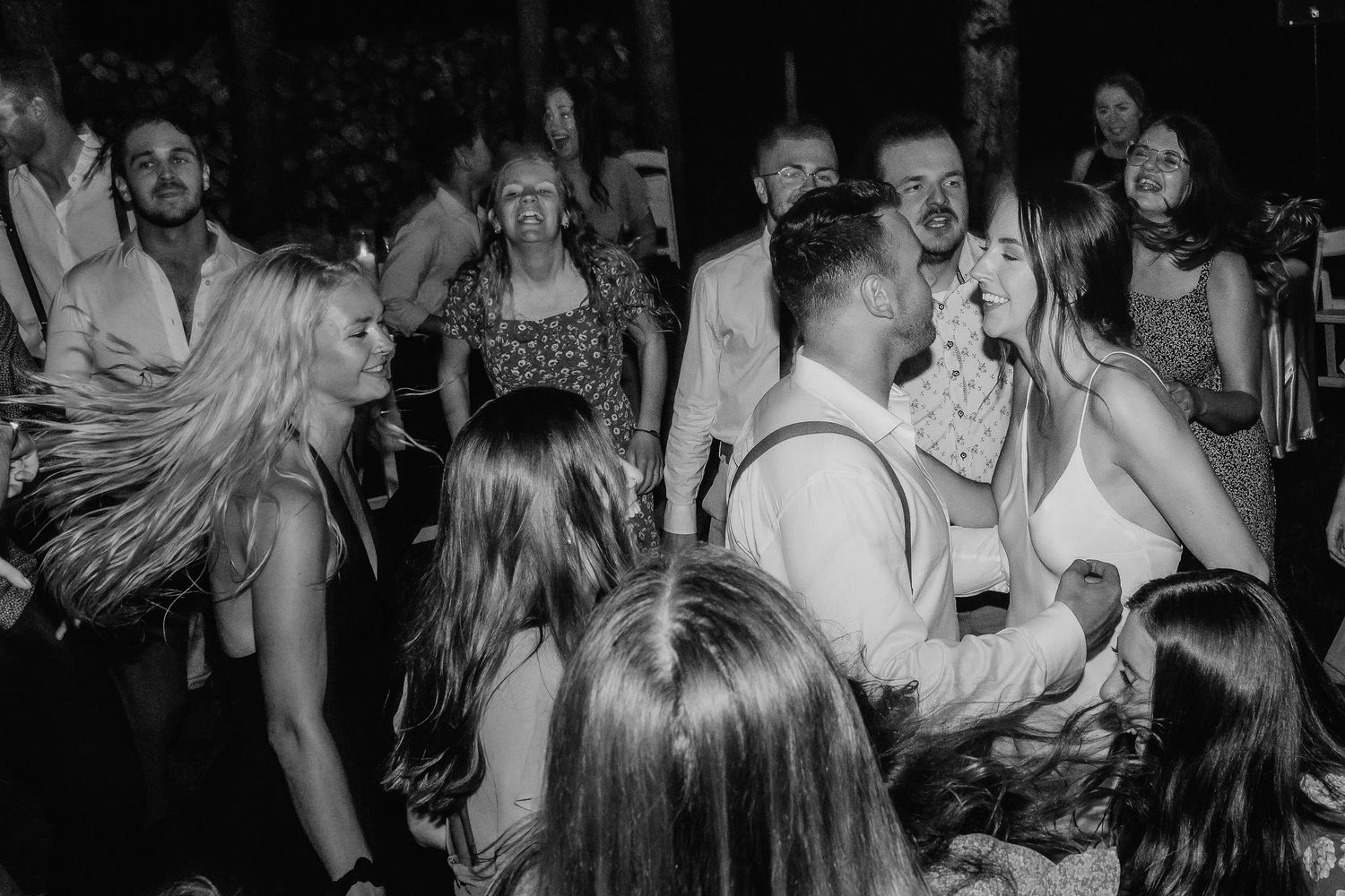 Black and white photo of people dancing and celebrating at a lively party or reception on the dance floor.