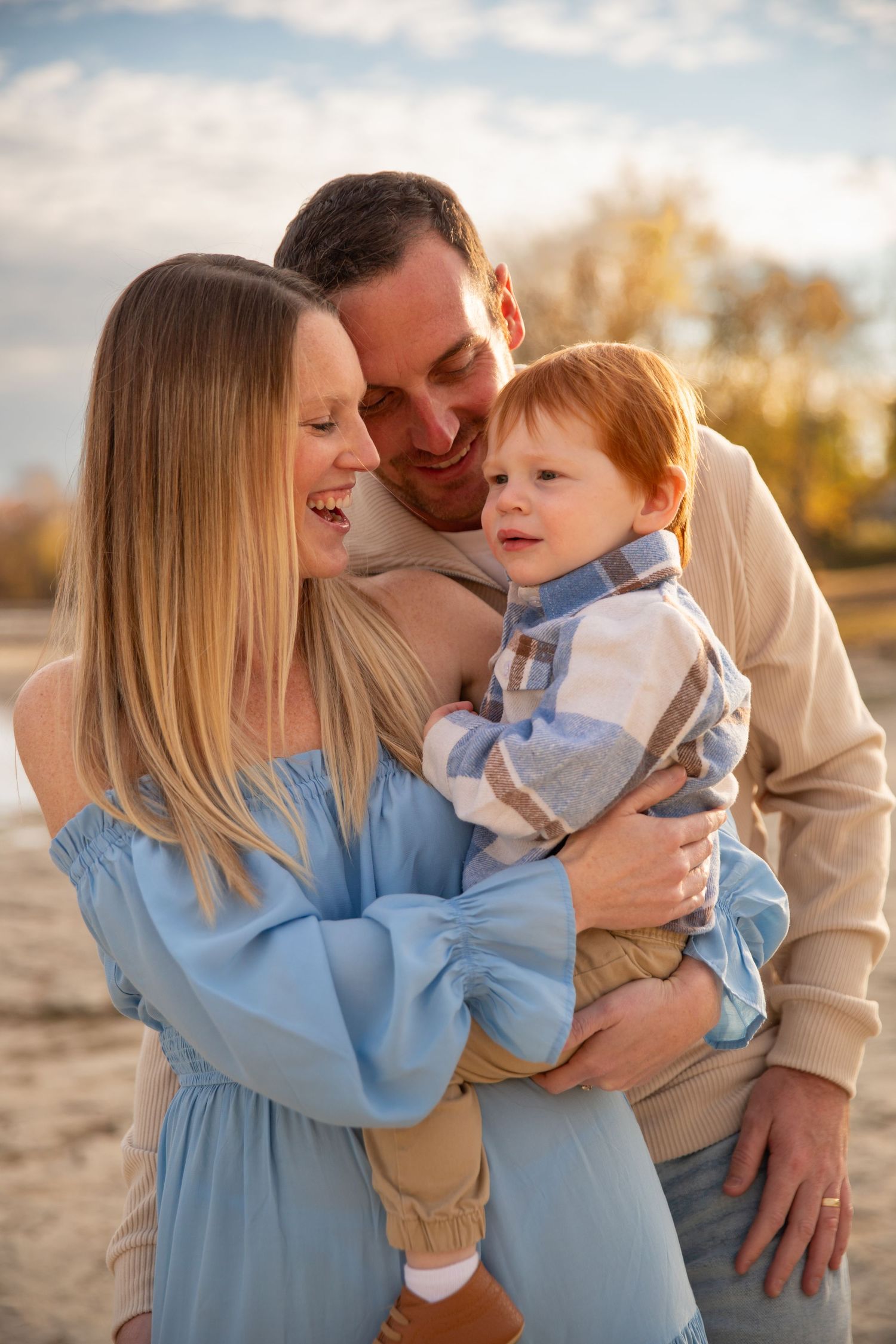 A family in coordinated blue and beige outfits shares tender moments together during an outdoor sunset photoshoot.