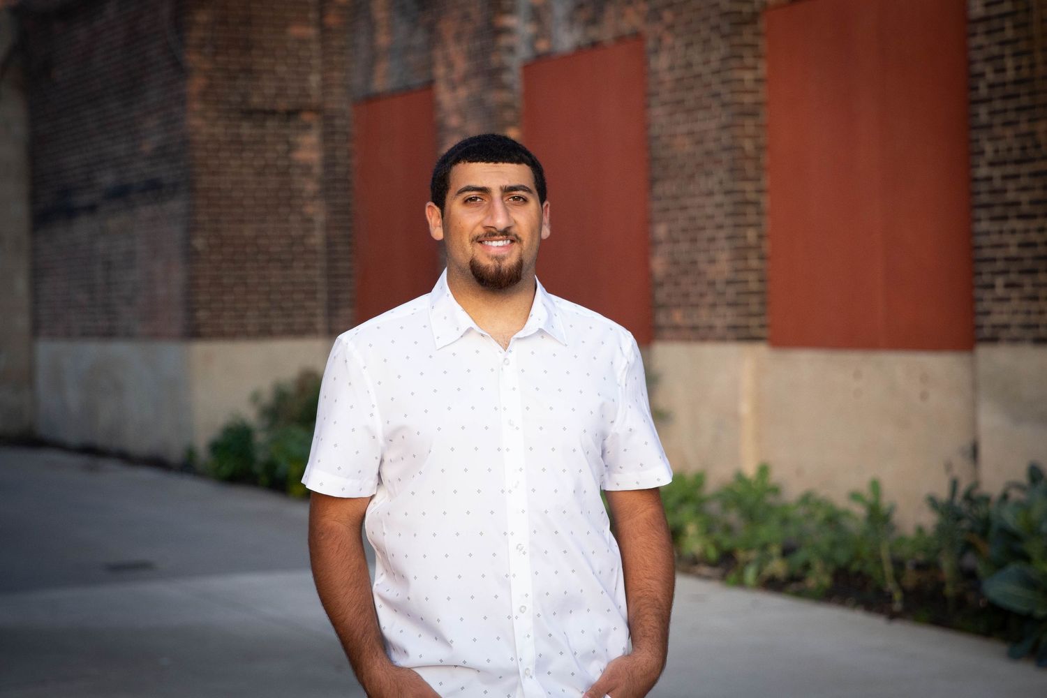 Person in white polo shirt smiles while standing against brick wall background.