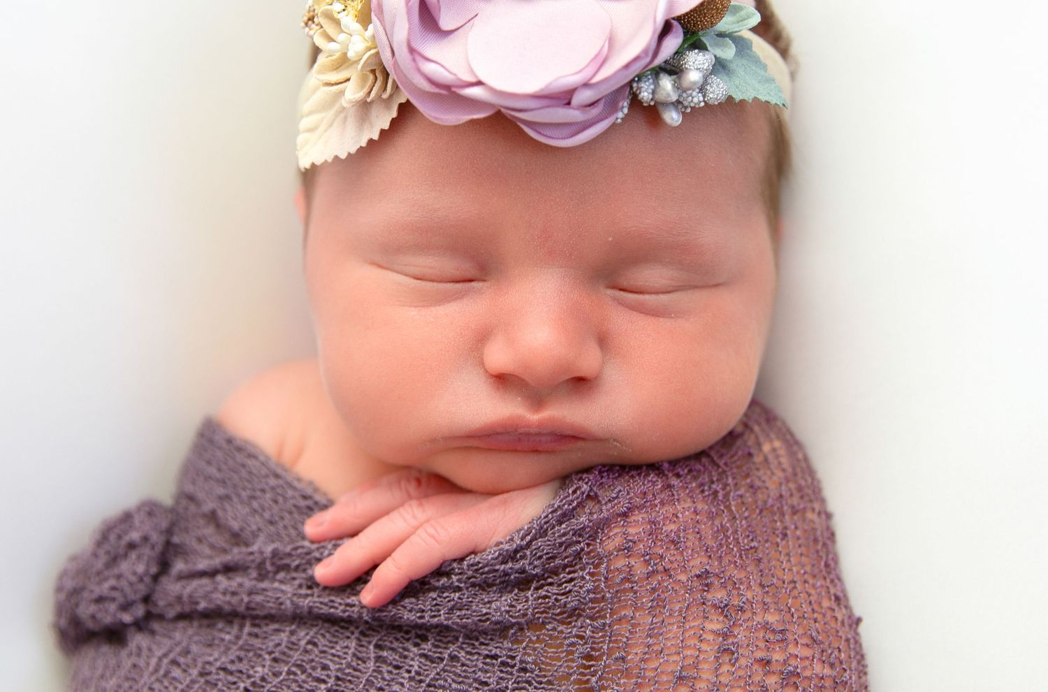 Sleeping newborn with purple flower crown and textured wrap.