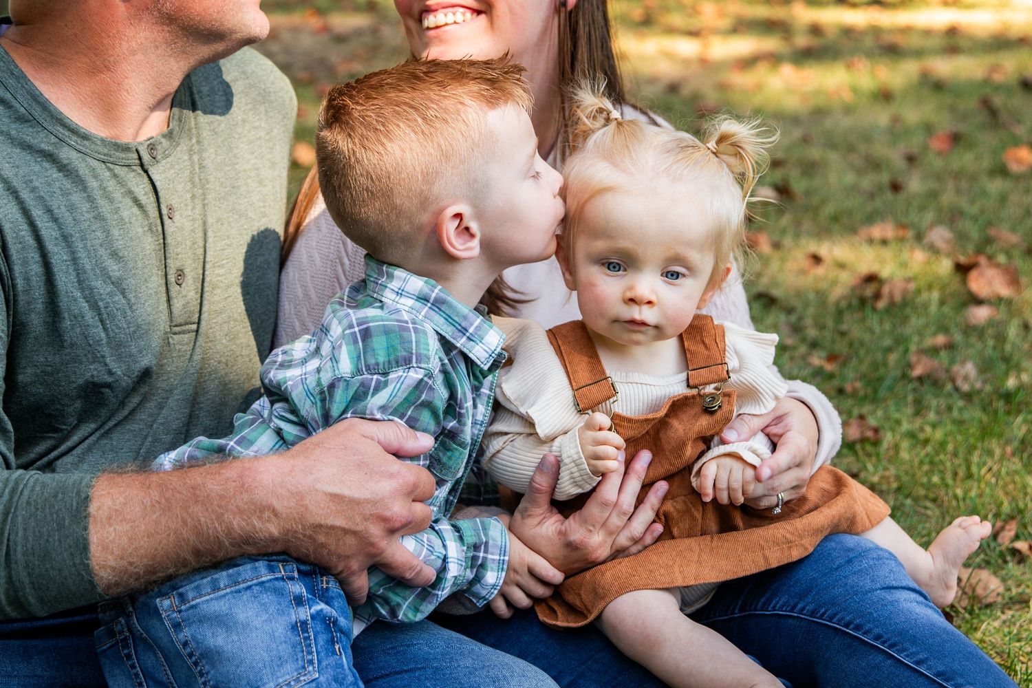 Family sitting together on grass during autumn with fallen leaves in background.