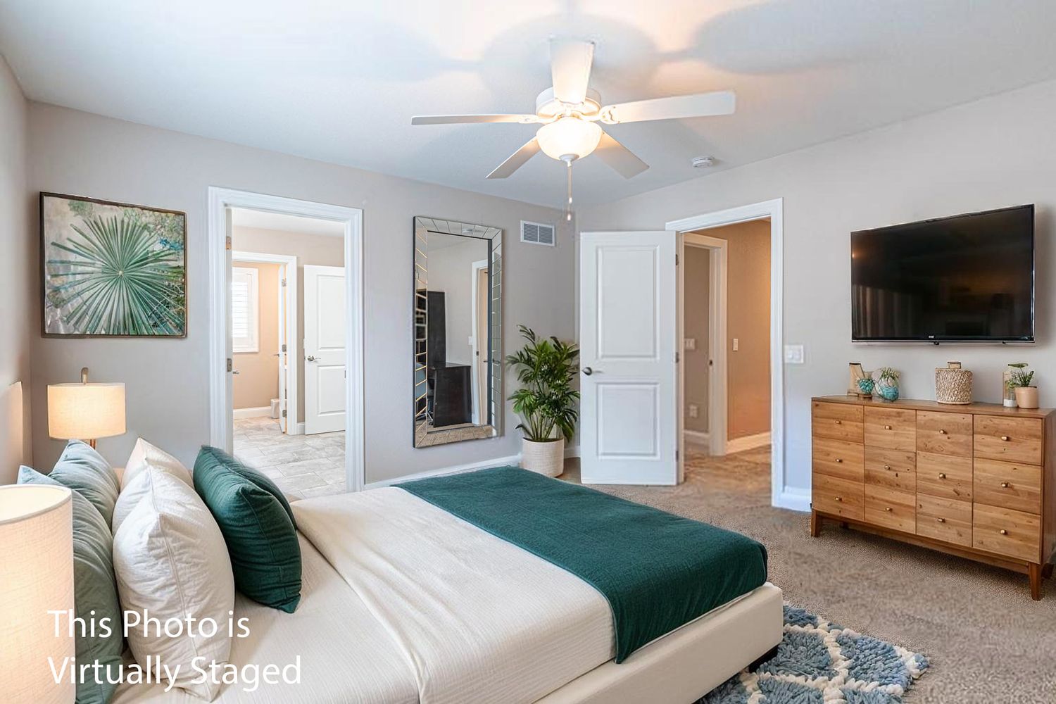 A bright and spacious bedroom with teal bedding, wooden furniture, and a ceiling fan in a modern home setting.