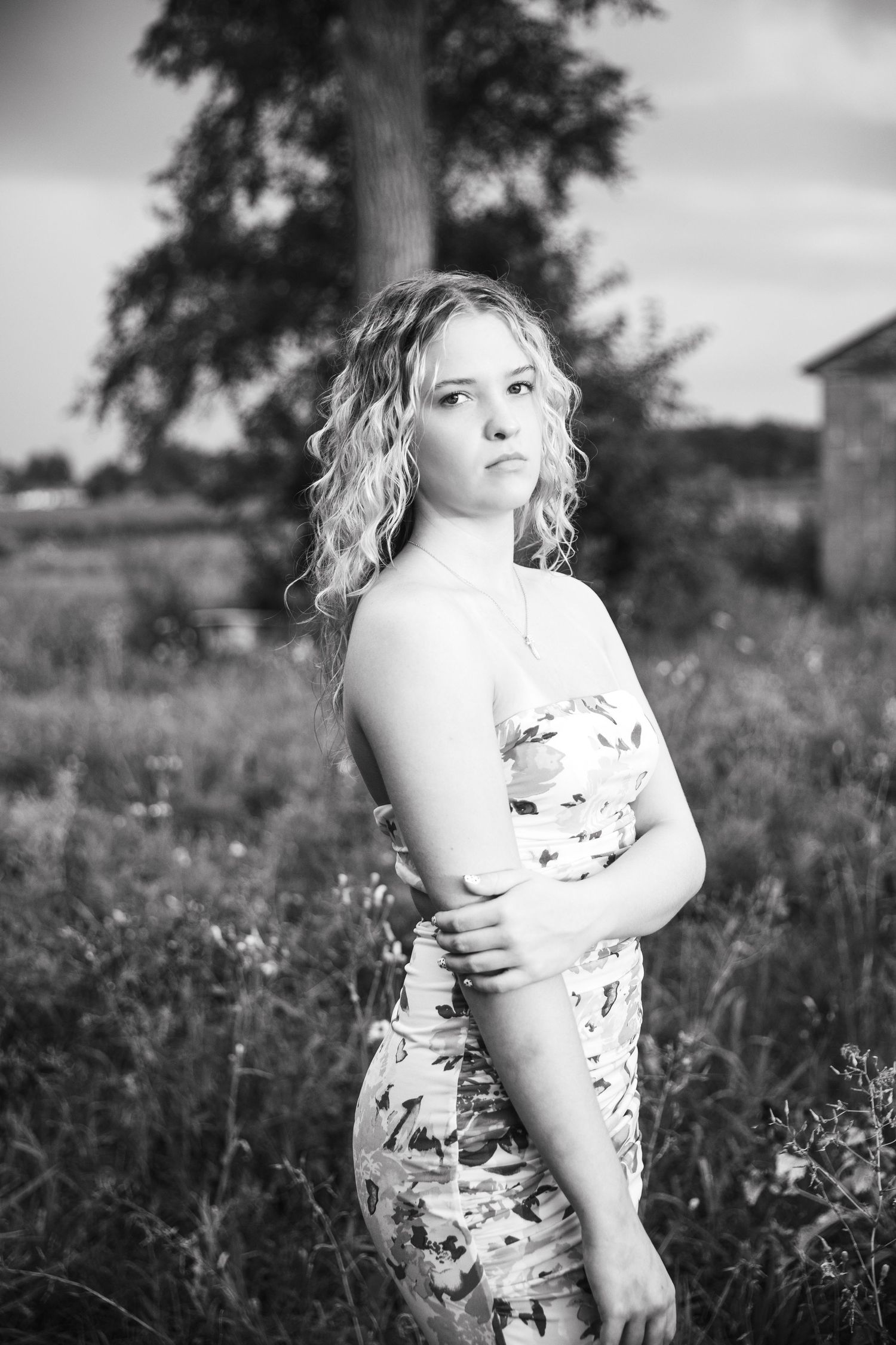 Black and white portrait series of a person in a floral dress sitting in a wildflower field.