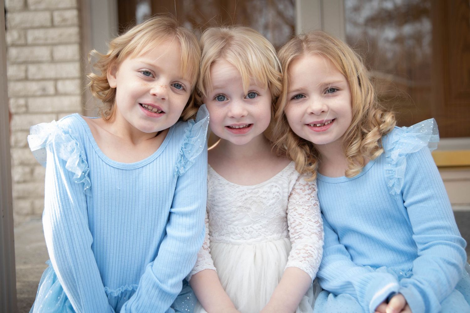 Three young children in coordinating blue and white outfits sitting together on brick steps.