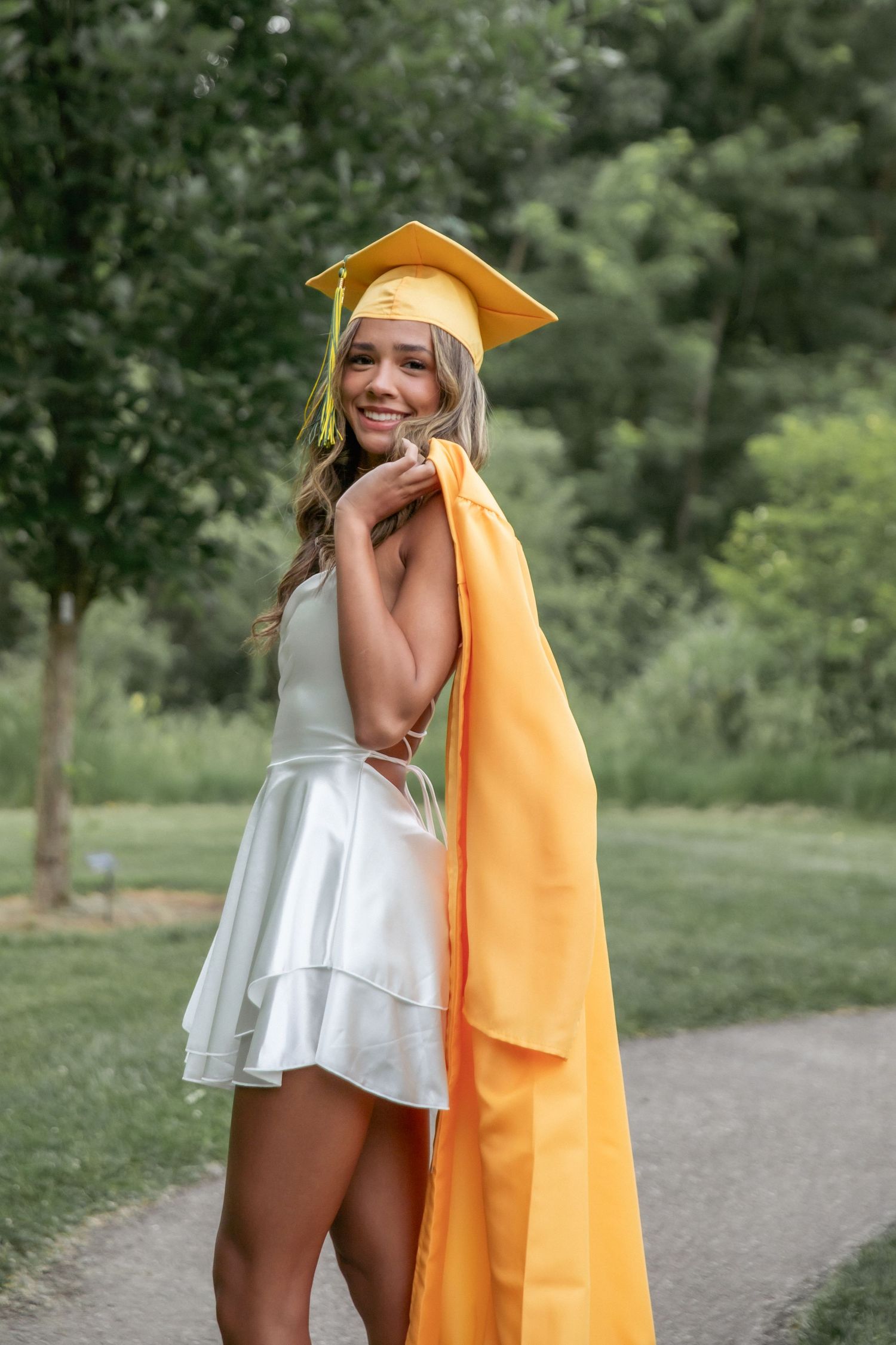 Graduation photos in white dress and gold cap with playful poses outdoors.