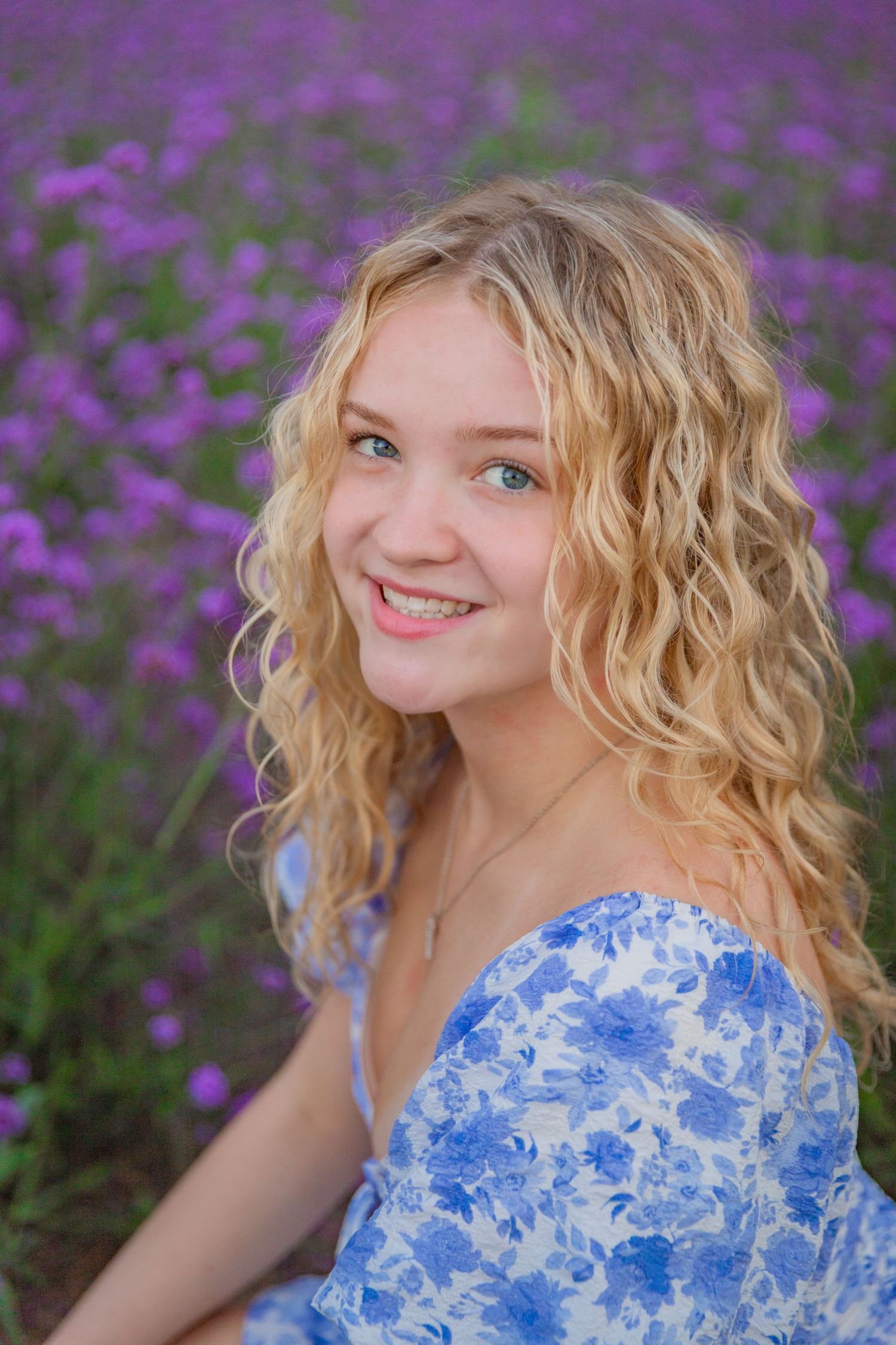 Portrait series in purple flower field with blue floral dress and natural curls.