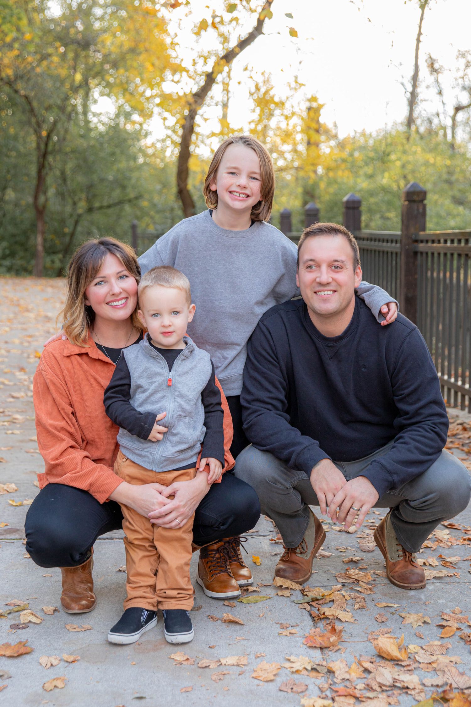 Family sitting together on autumn leaves with casual outfits and warm smiles.