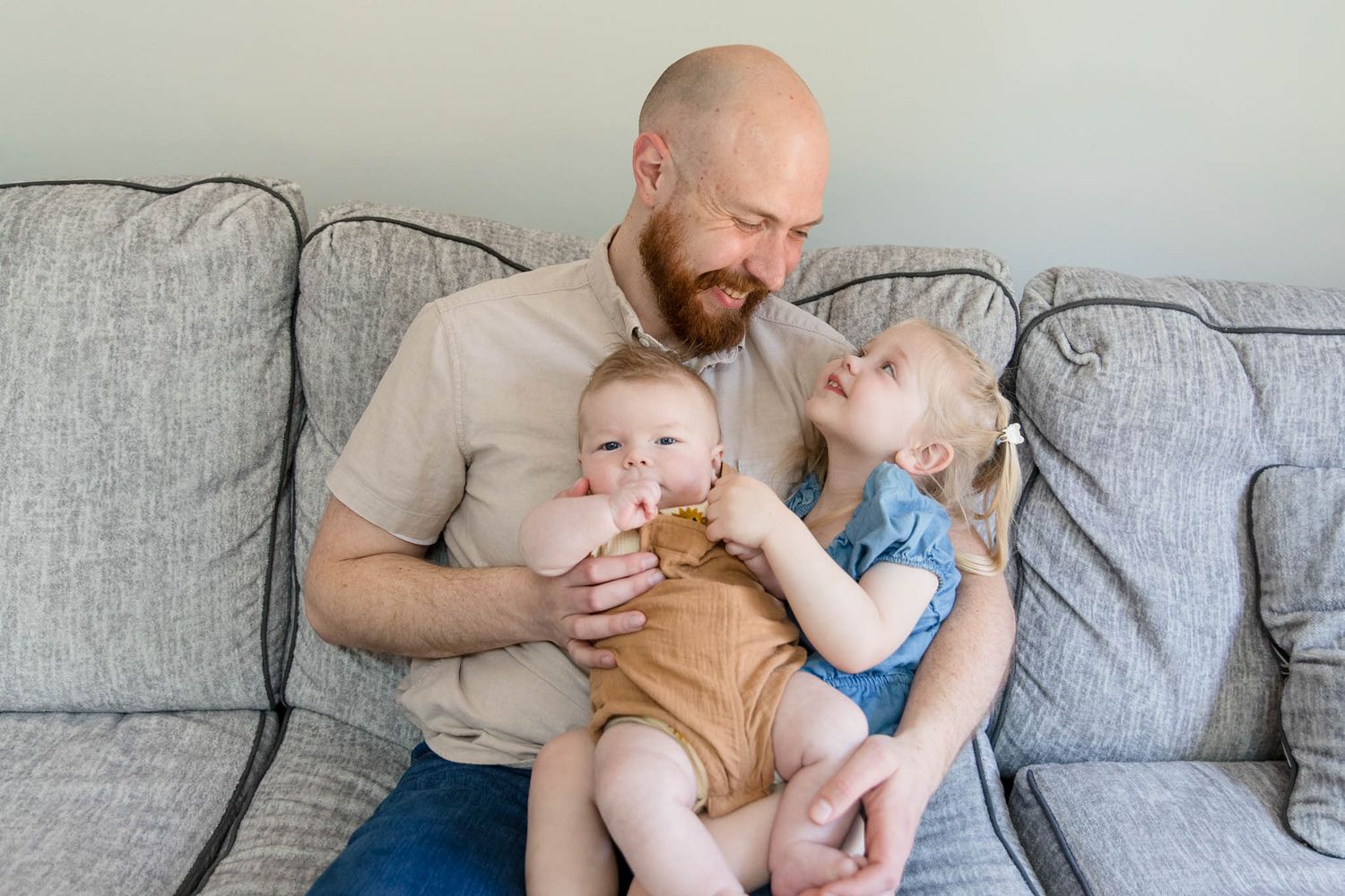 Candid lifestyle moments of a family relaxing together on a grey couch at home.