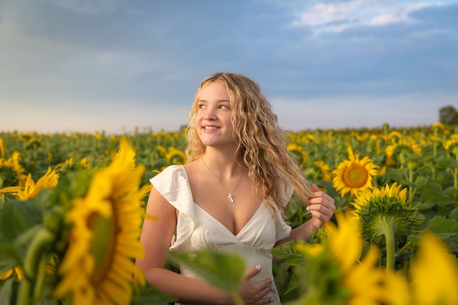 Woman in white dress poses joyfully in a vibrant field of blooming sunflowers on a sunny summer day.