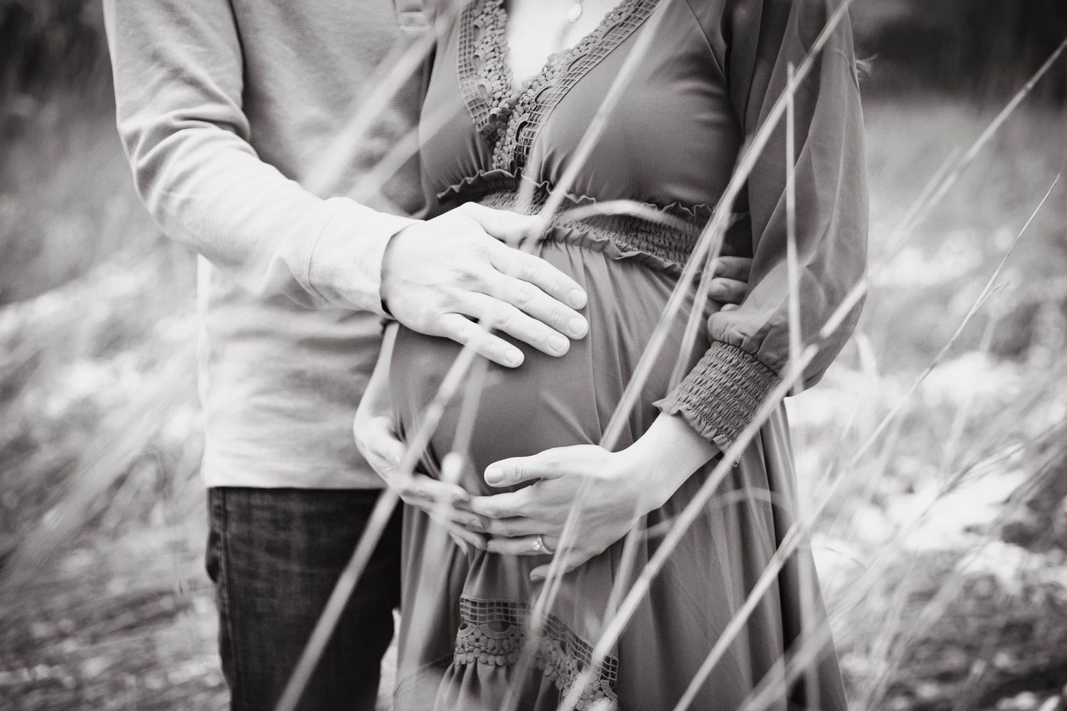 Artistic black and white maternity photos in tall grass field.