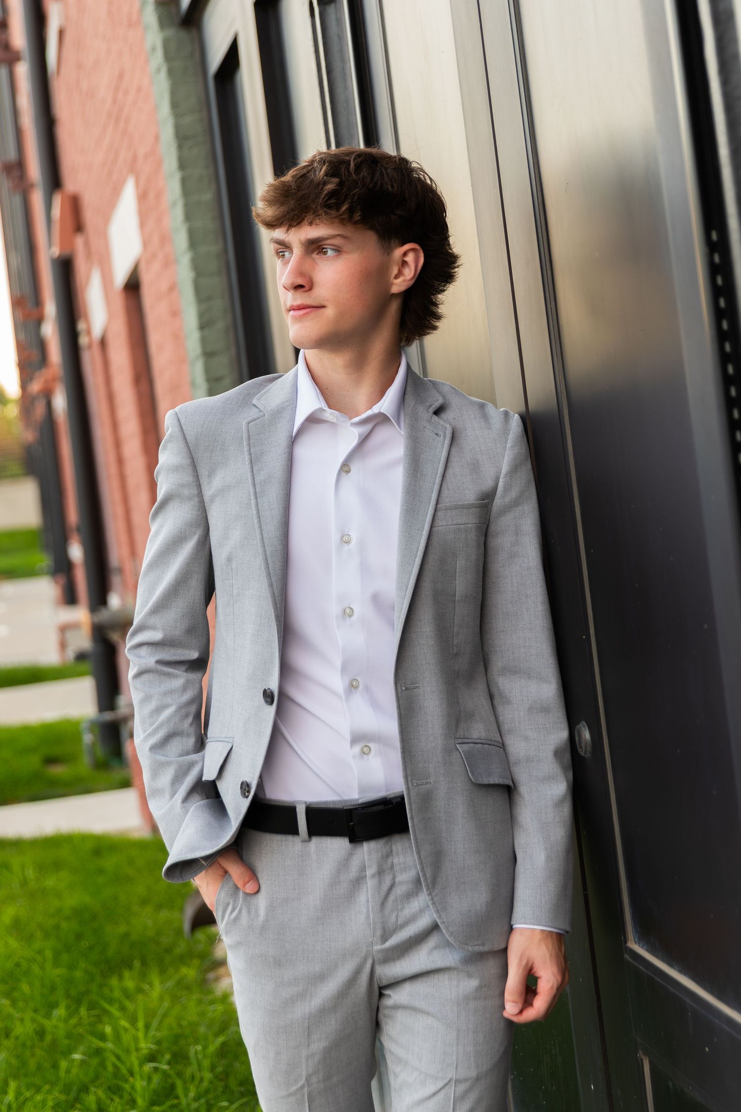 Young person in gray suit and white shirt posing against modern building exterior.