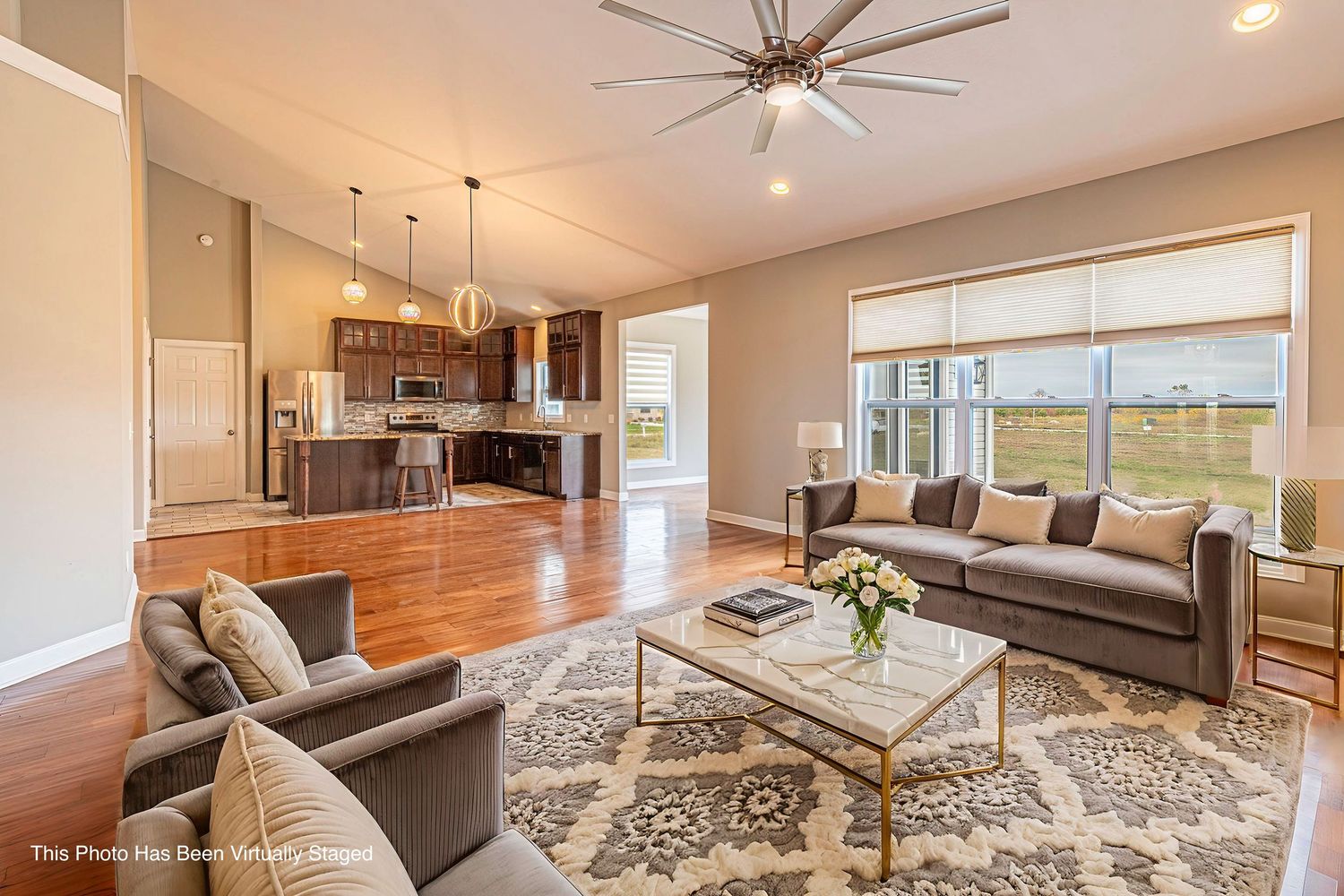 Modern open concept living room with hardwood floors, gray sofa, patterned rug and large windows overlooking scenic views.