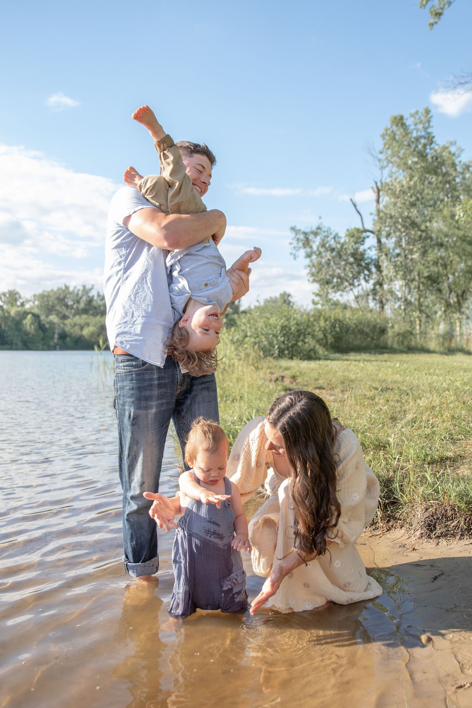 Family playing and splashing together at the edge of a lake on a sunny day.