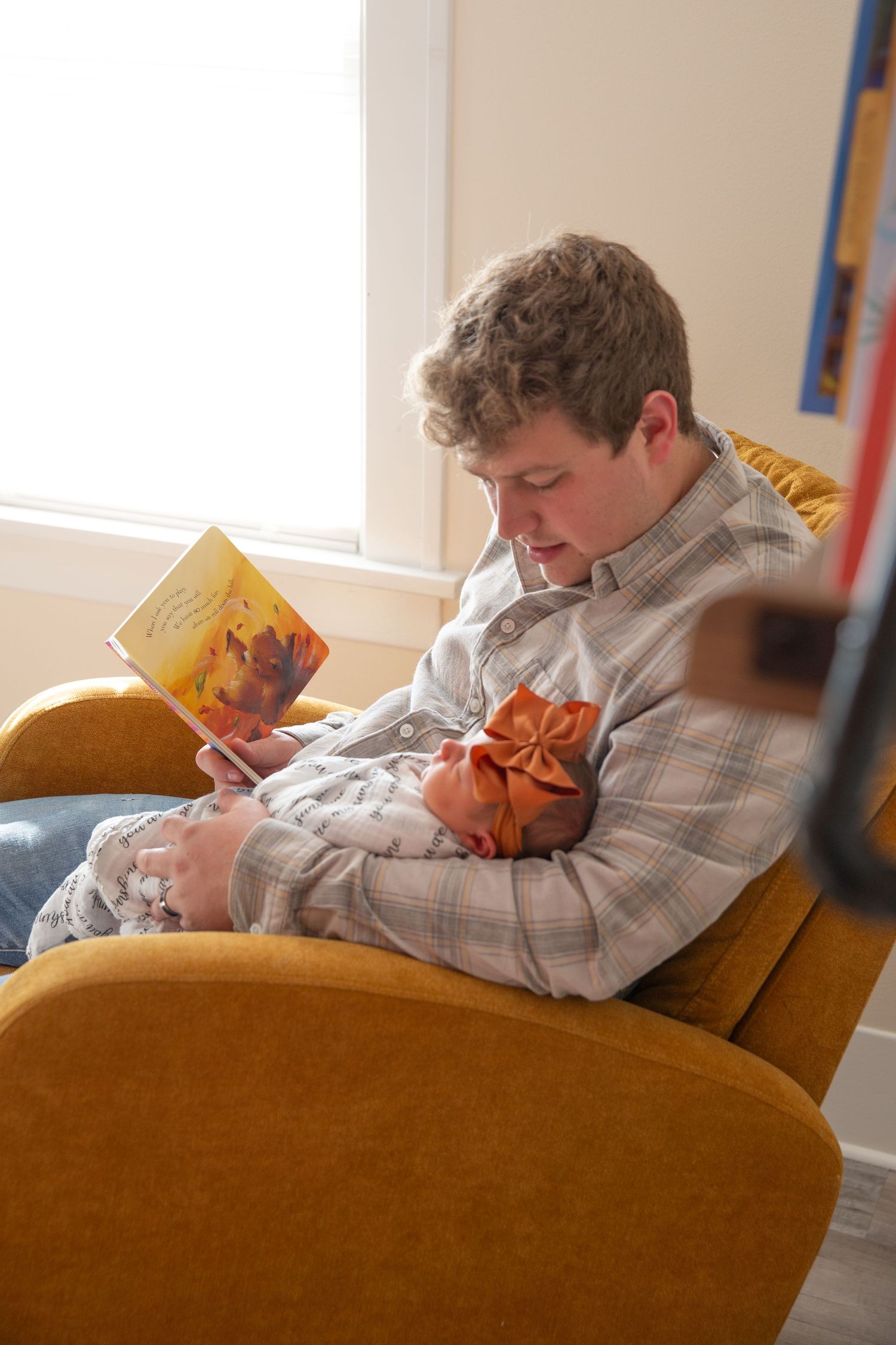 Person reading book while sitting in orange armchair with baby.