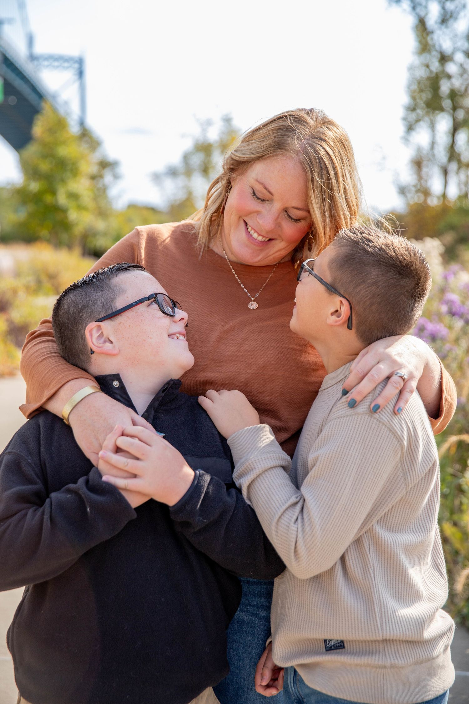 Family sharing playful hugs and laughter in a sunny outdoor setting with casual sweaters.