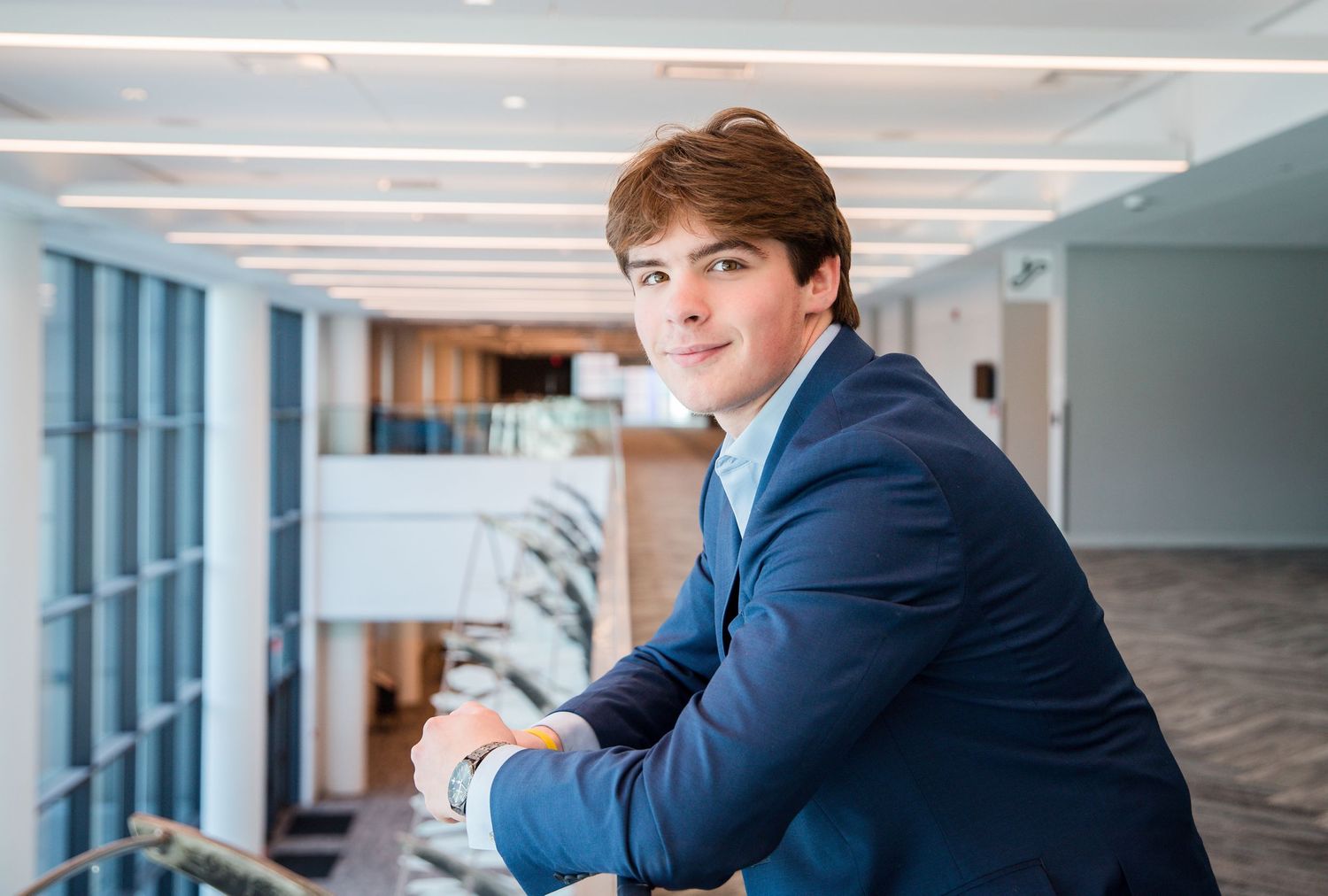 Young professional man in blue blazer posing confidently in modern office building atrium.