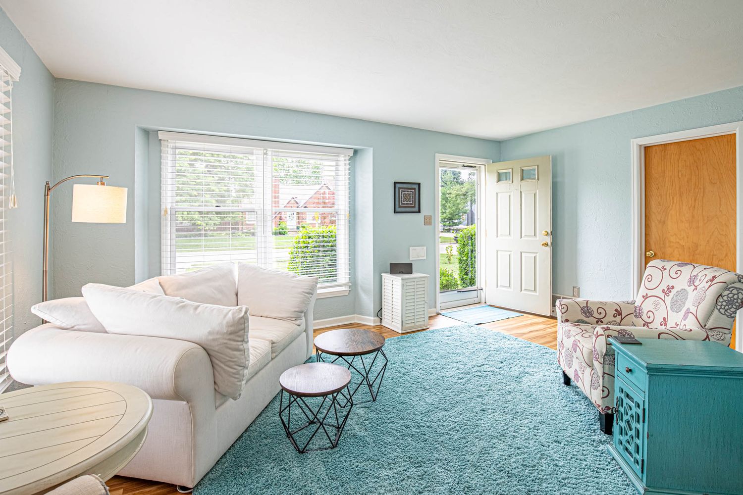 A panoramic view of a bright coastal-themed bedroom with turquoise walls and white bedding in natural light.