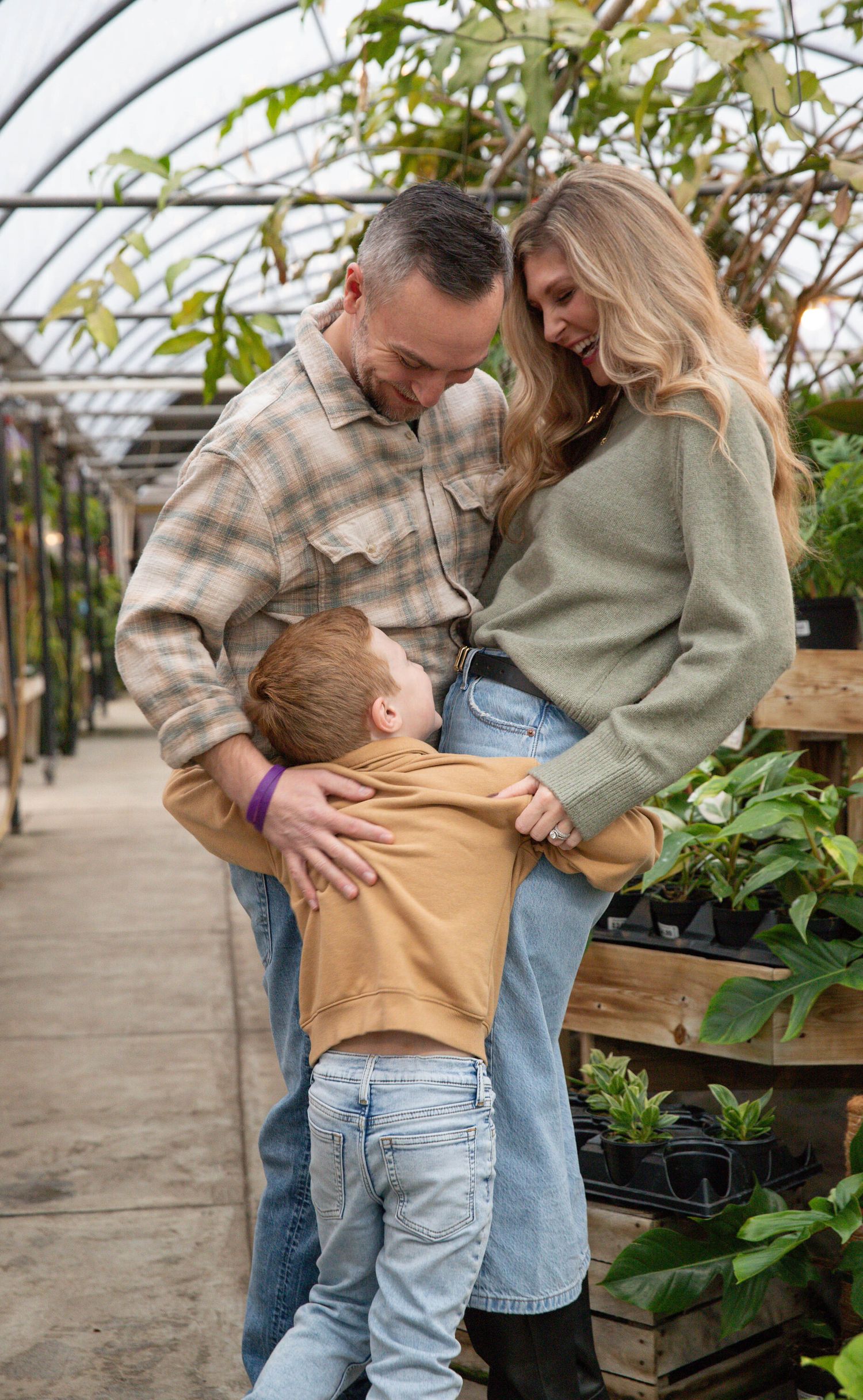Family sharing playful moments together in a greenhouse setting with natural light.