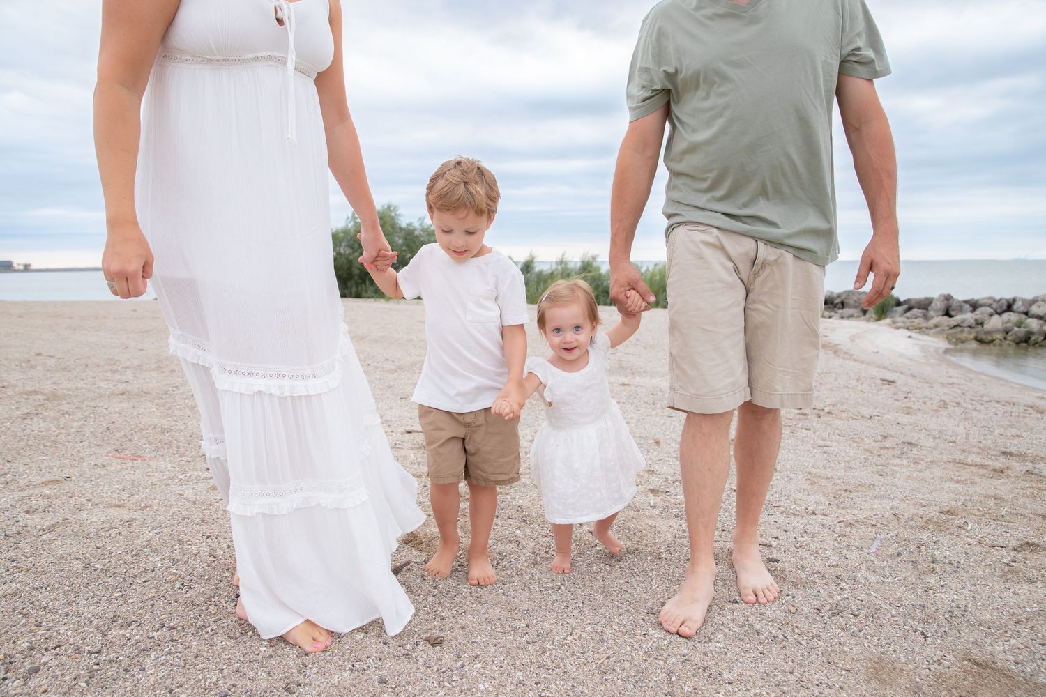 Family walking together barefoot on a sandy beach on a cloudy day.