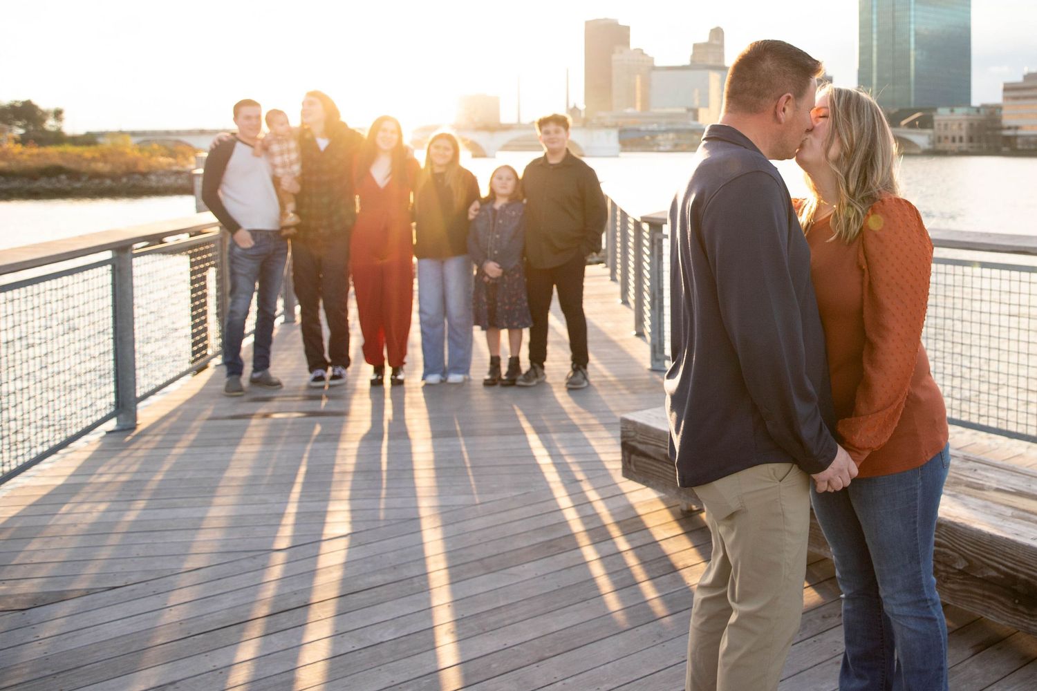 Silhouettes of people walking along waterfront boardwalk during golden sunset.