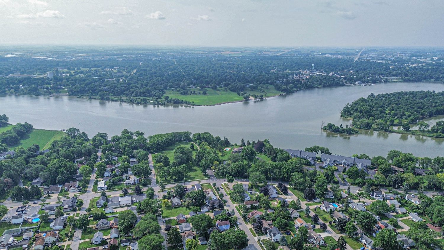 Aerial panoramic view of a riverside community with residential homes and green spaces nestled along the shoreline.