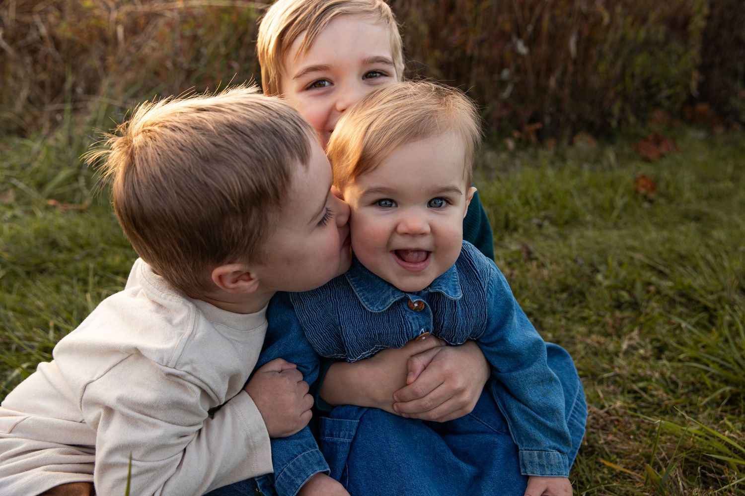Two children share a sweet moment together while sitting in grass during an outdoor photo session.